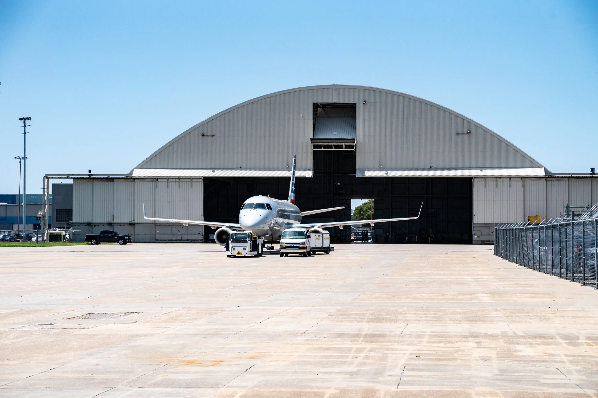 Airplane on tarmac outside large hangar with loading dock, clear blue sky.