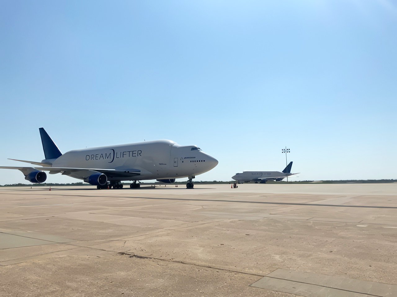 A large white airplane labeled 'DREAM LIFTER' parked on an airport tarmac with another smaller airplane in the background.