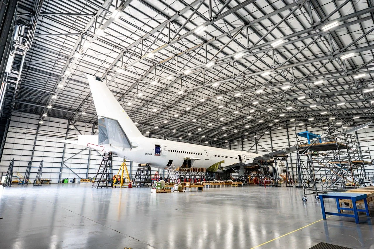 Inside an aircraft hangar with a large airplane under maintenance, surrounded by scaffolding and maintenance equipment.