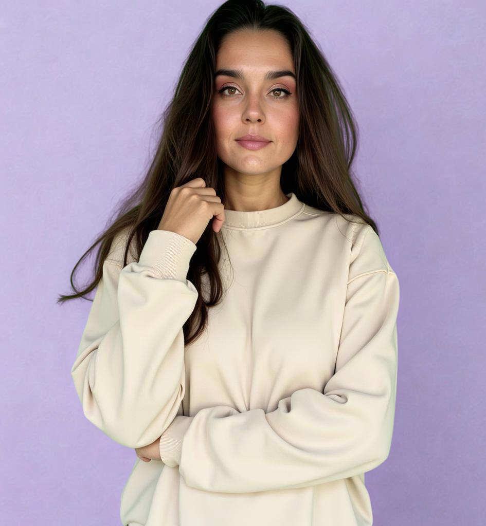 Mujer joven con cabello largo y oscuro, vestida con sudadera beis, posando contra fondo lila.