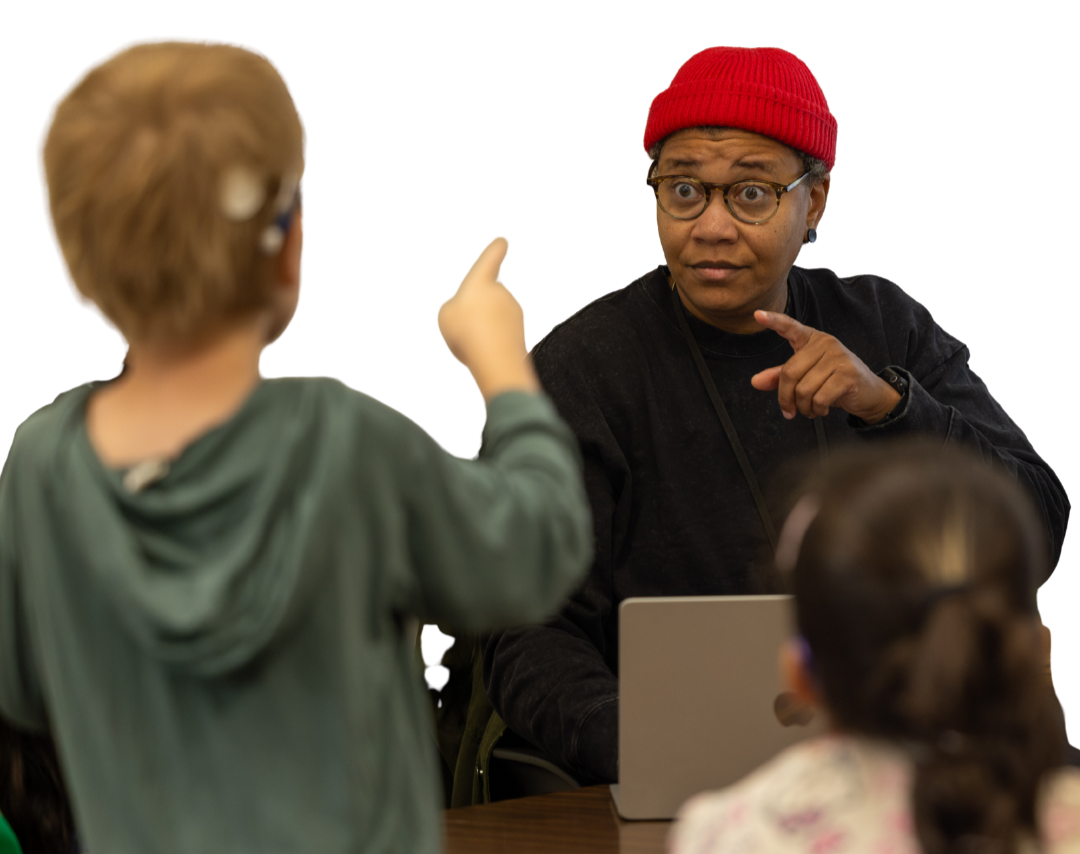 Miki signs and interacts with young children seated at a table during a small group learning activity.