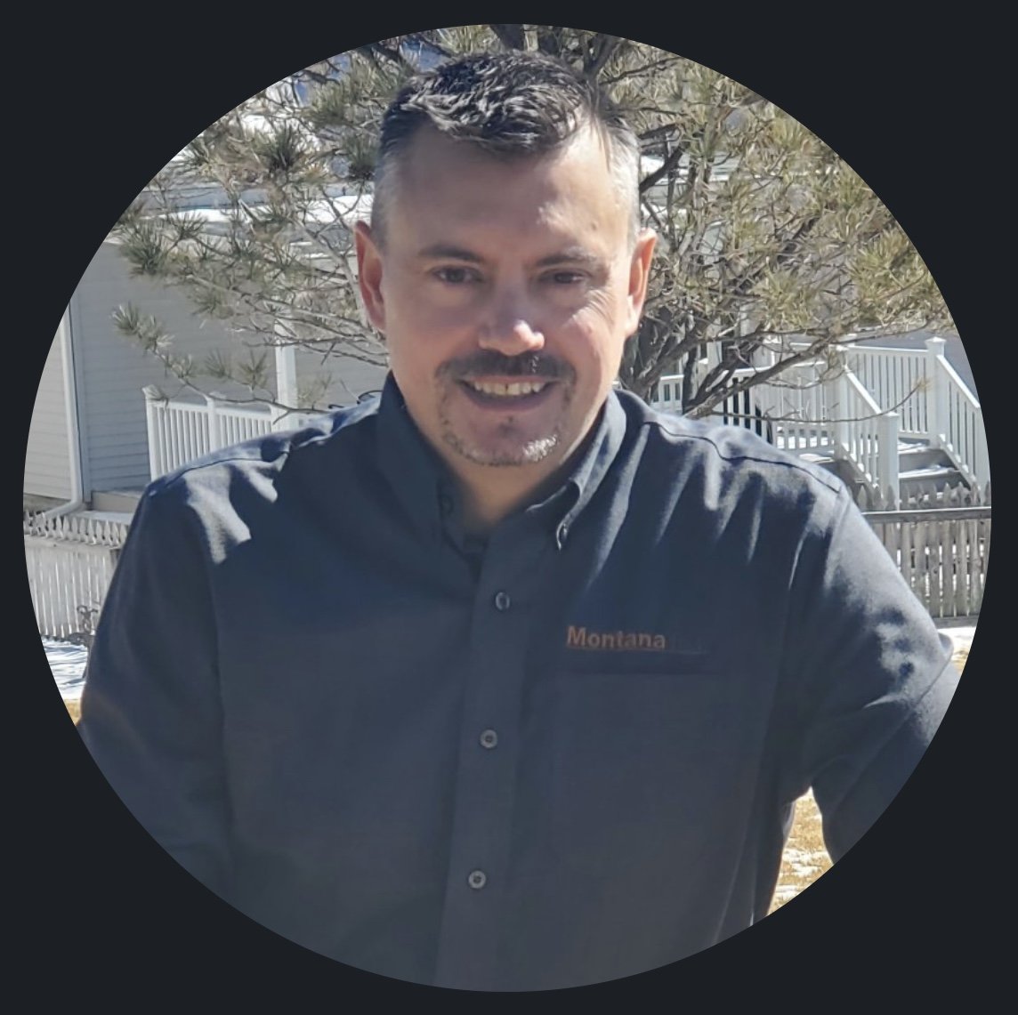 A man smiling outdoors with a tree and suburban houses in the background.