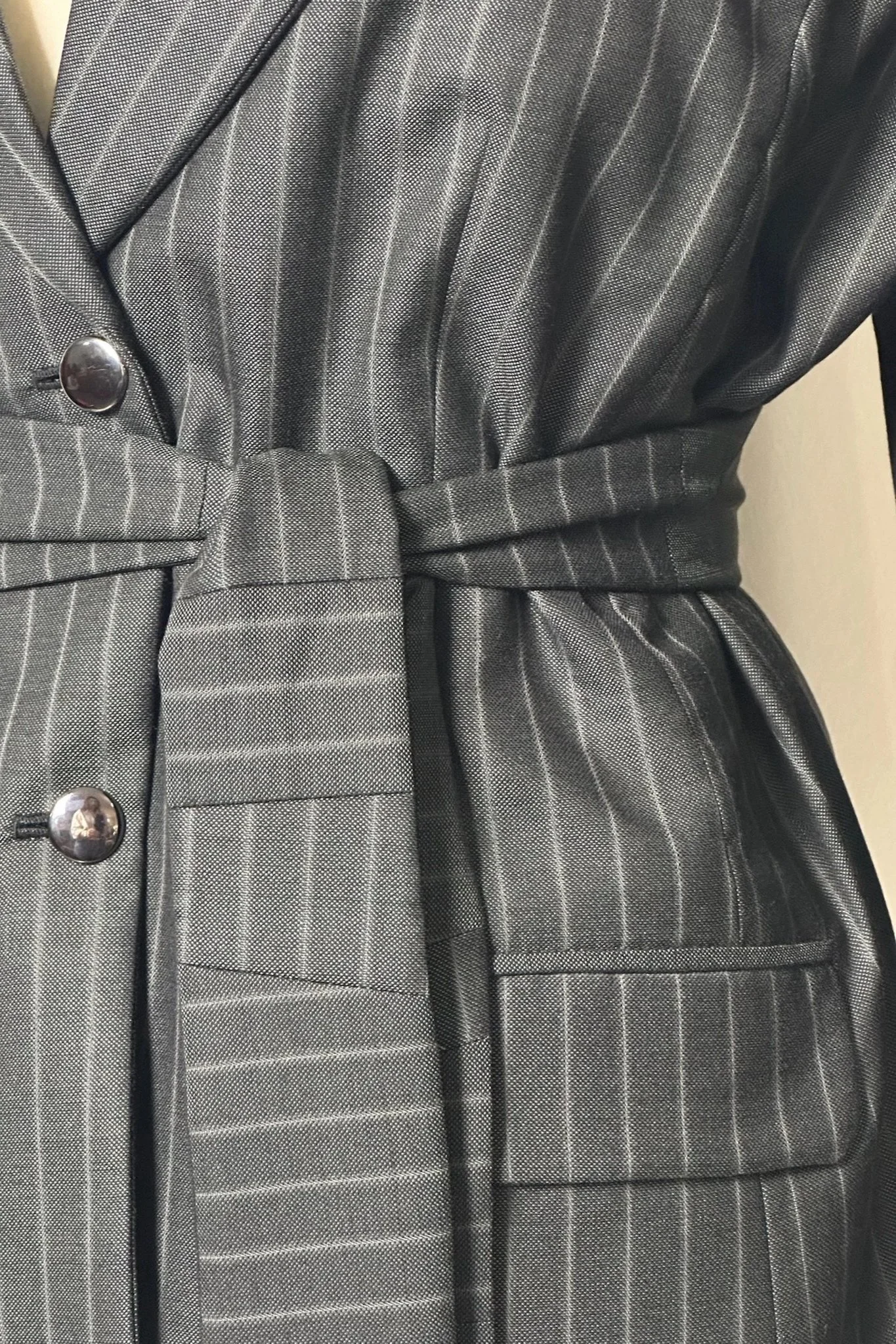 Veste grise à rayures fines, cintrée avec ceinture assortie, boutons métalliques, tissu à motif pied-de-poule.
