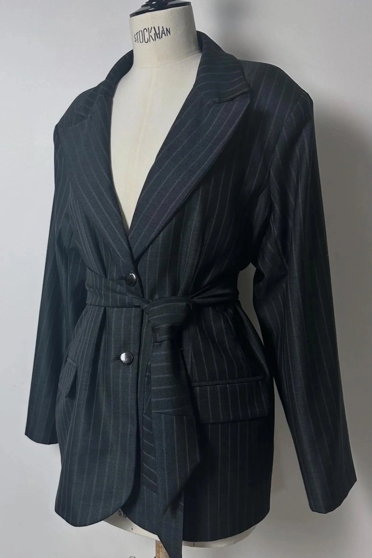 Manteau à motifs à rayures sur une mannequin, porté avec un col large et une ceinture à la taille, en tissu sombre.