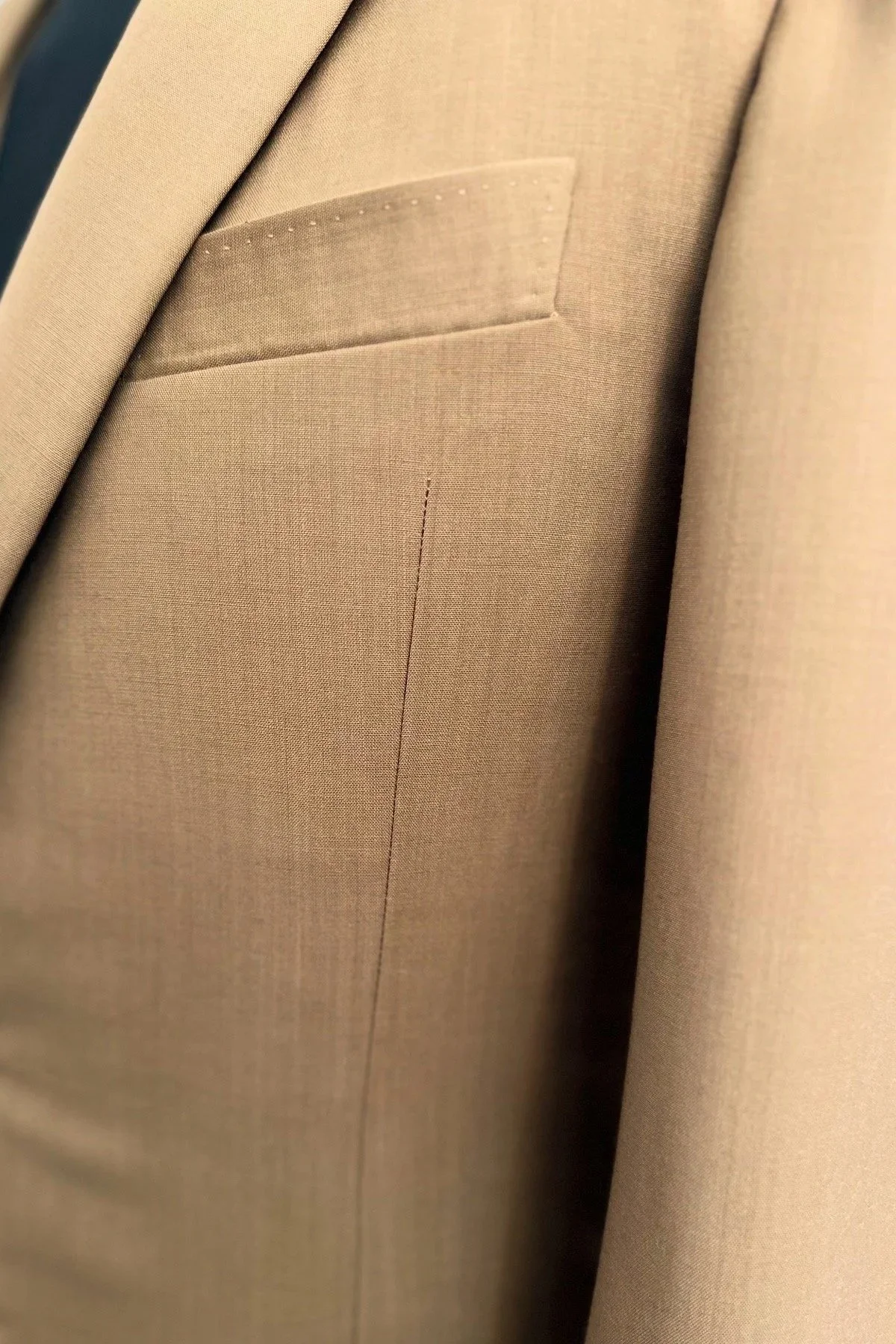 Détail d'un tissu beige de costume avec une poche et une couture visible.