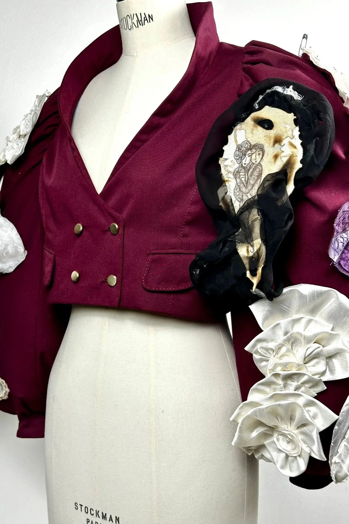 Une robe de style vintage bordeaux avec des détails en tissu blanc et noir, portant une broderie d'une femme sur l'épaule, sur un mannequin blanc sans visage.