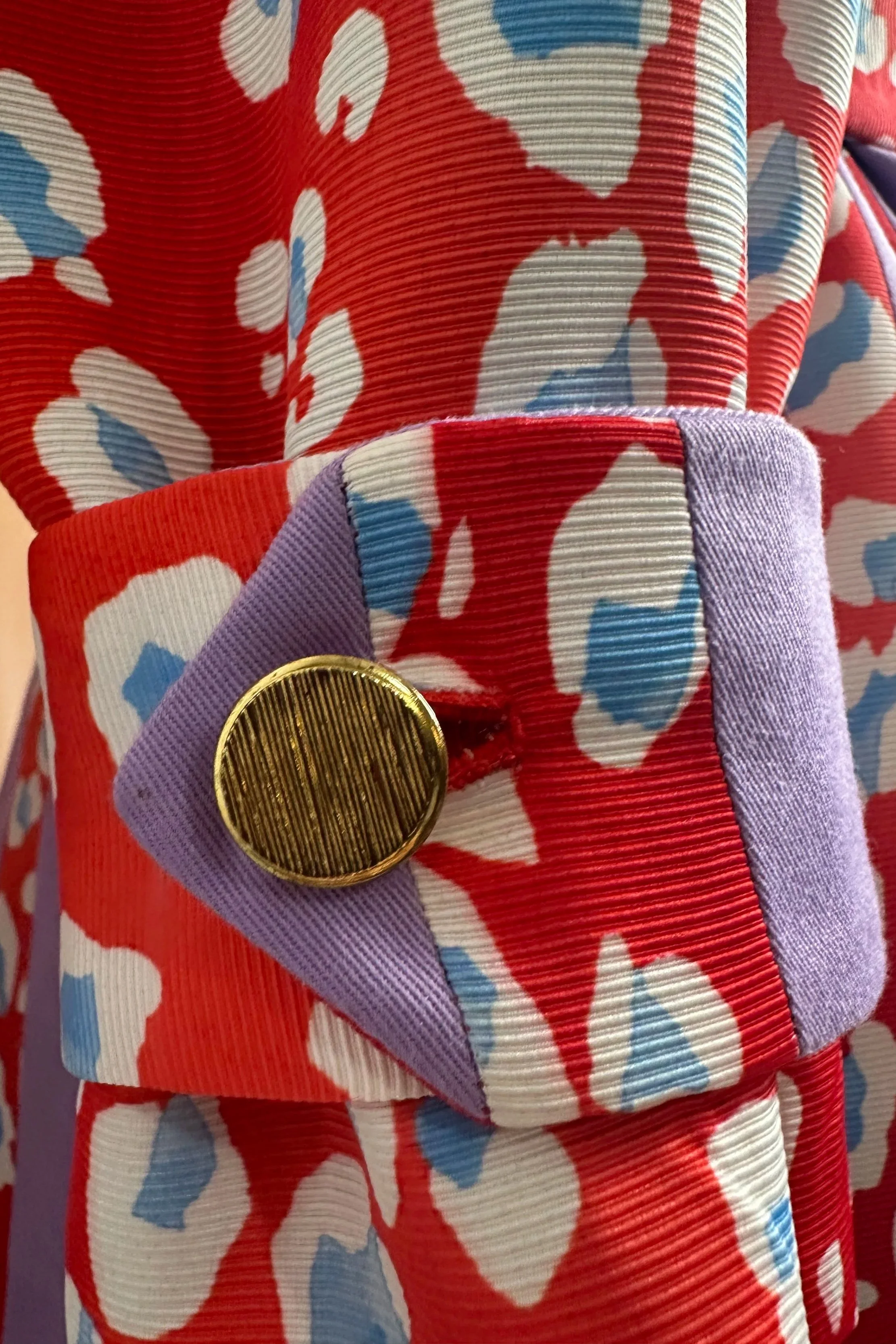 Un vêtement coloré avec un motif floral rouge, blanc, bleu et violet, avec une boucle dorée et un détail violet en tissu.
