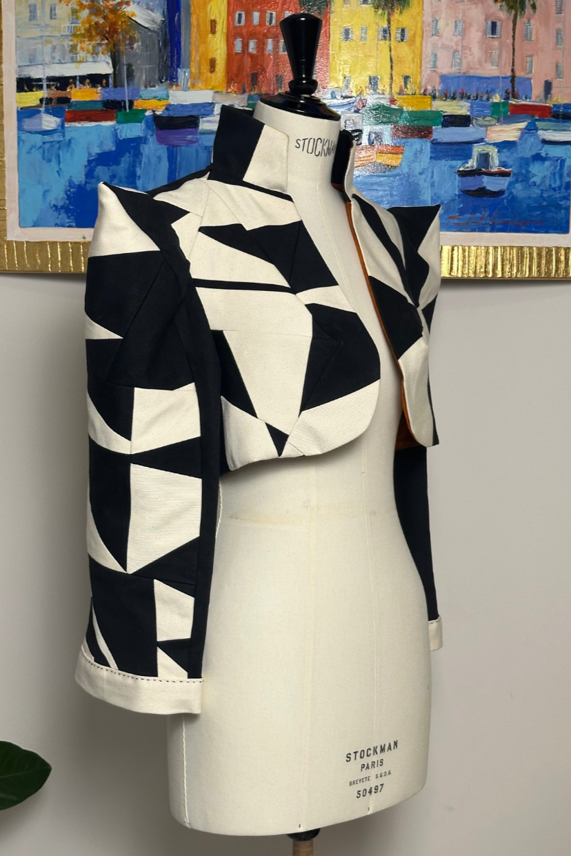 Vêtement à motif géométrique noir et blanc sur un mannequin dans une pièce, tableau coloré en arrière-plan.
