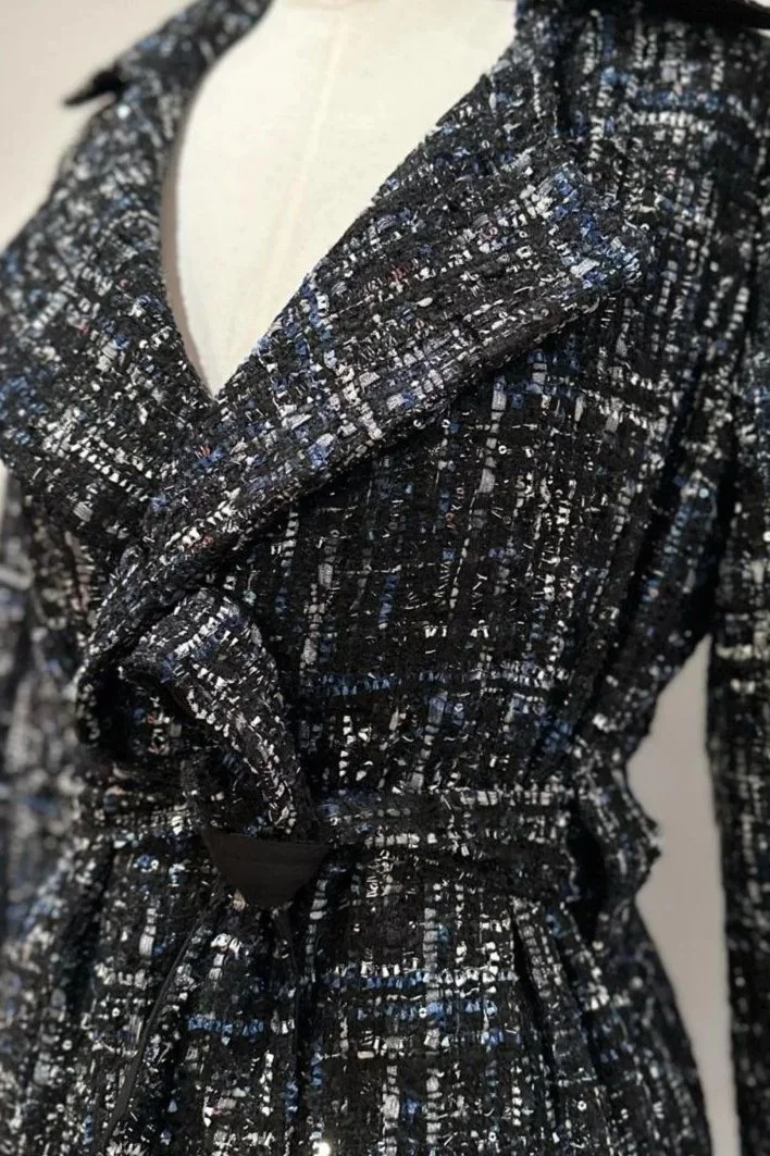 Manteau noir et blanc à motif tweed, noué à la taille avec une ceinture noire.