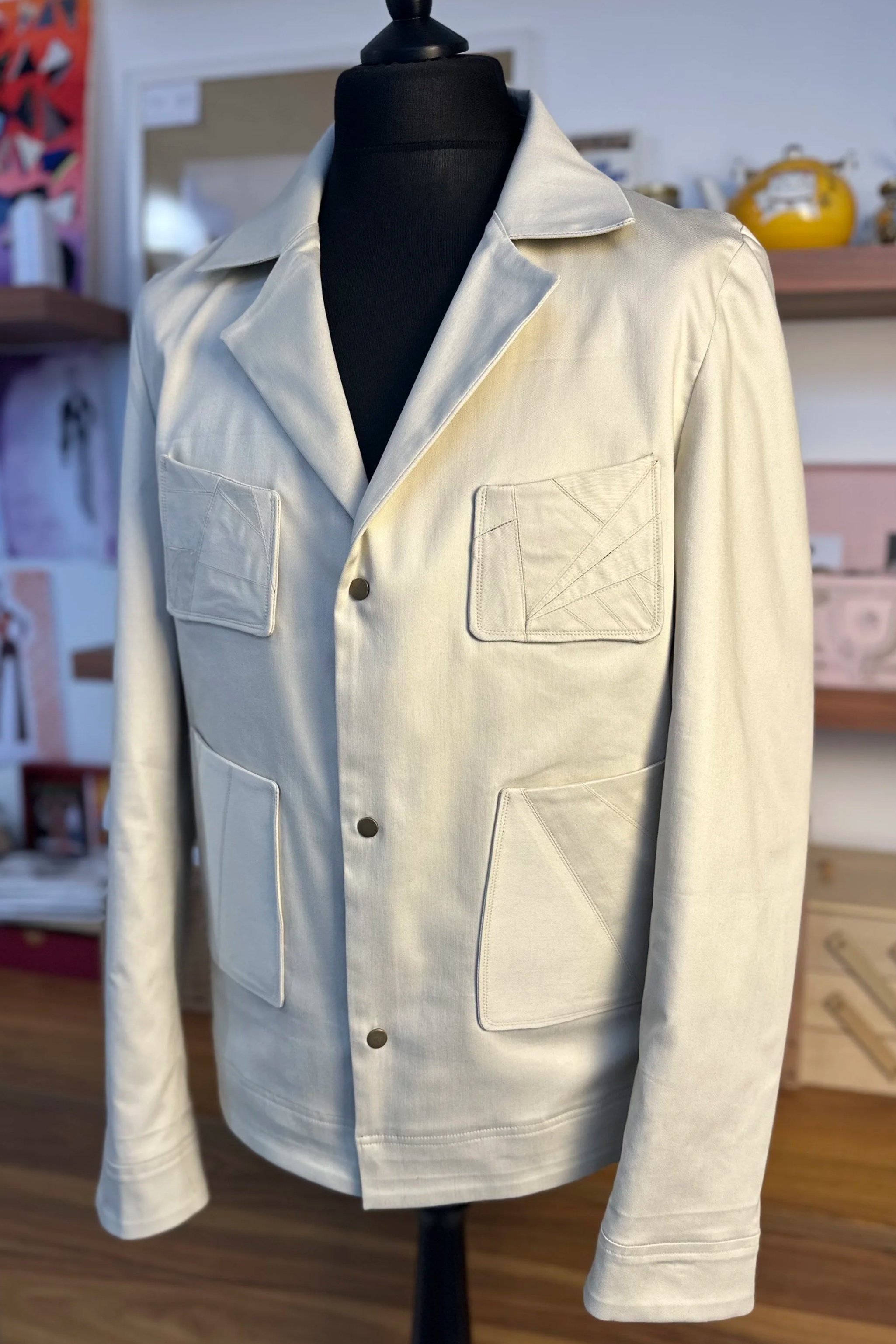 Veston blanc avec deux poches poitrine avec un motif géométrique, affiché sur un mannequin dans une boutique.