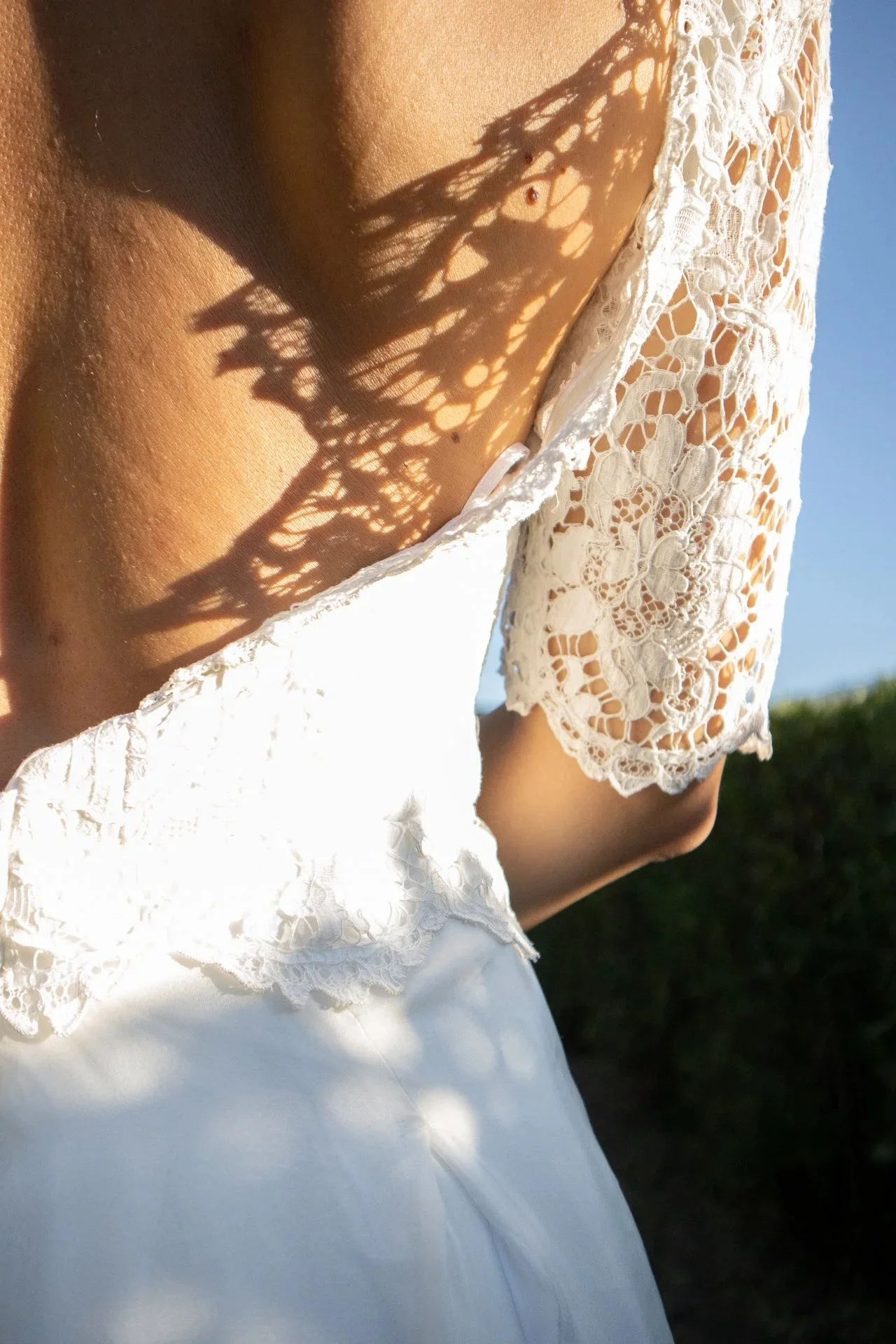 Une femme portant une robe blanche avec des détails en dentelle, en plein soleil, avec l'ombre de son chapeau en crochet tombant sur sa peau.