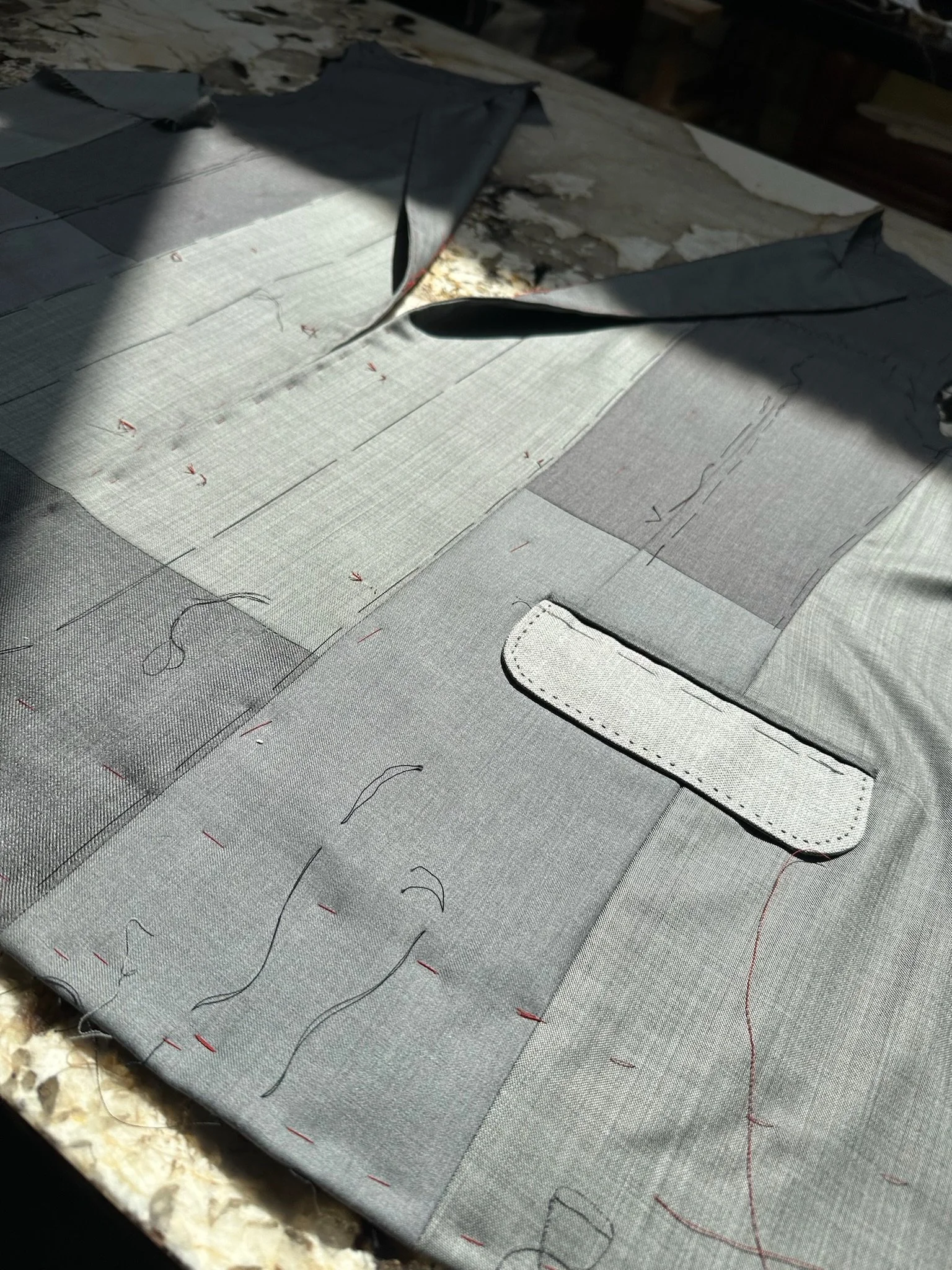 Devants d’une veste en patchwork gris en cours de montage, avec fils de bâti et poche à rabat.