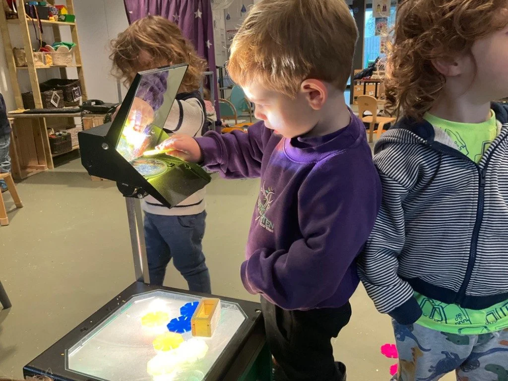 Children playing with an illuminated light box and sensory toys in a classroom.