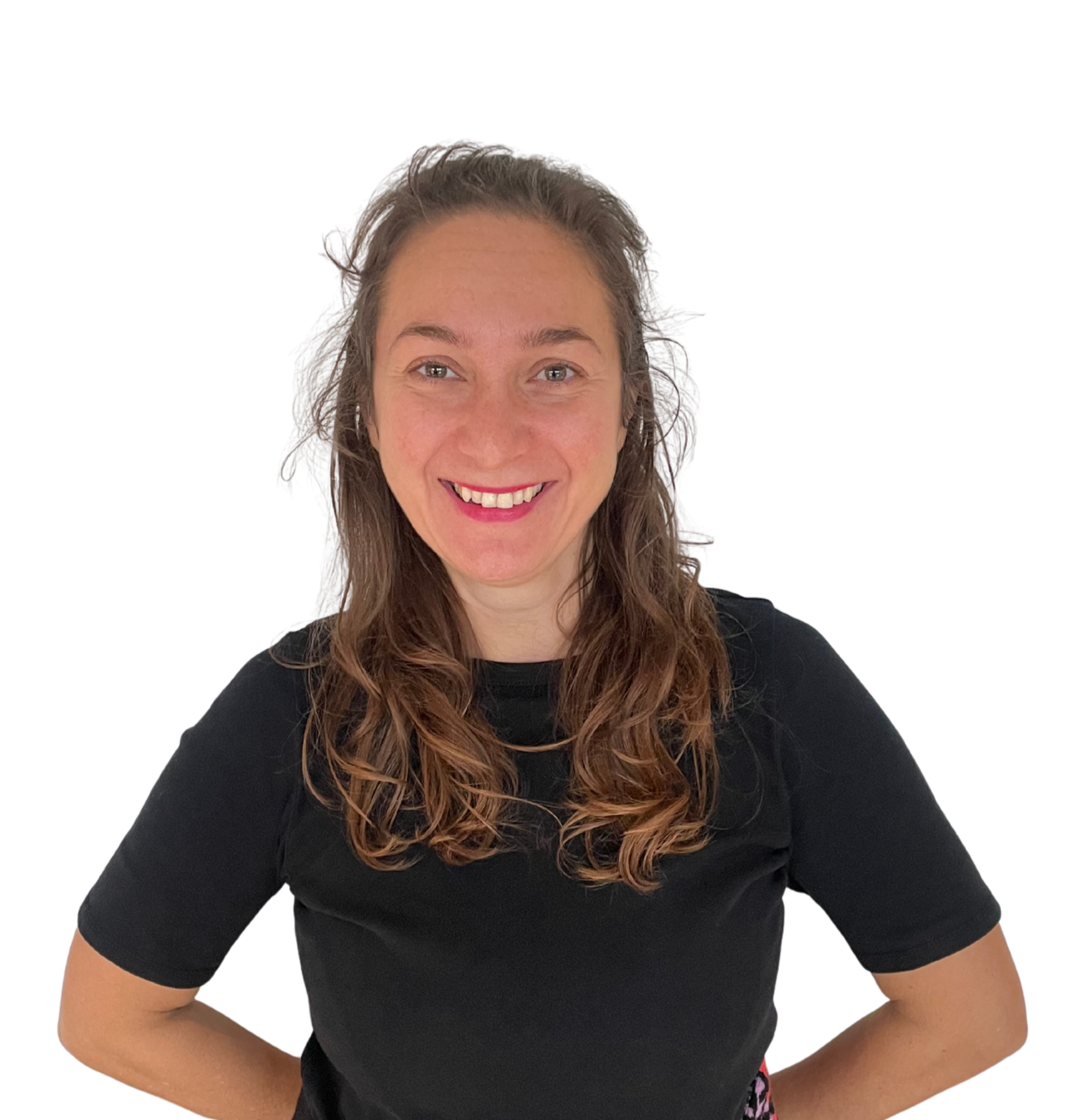 A woman with wavy brown hair, smiling, wearing a black shirt, posing with her hands on her hips.