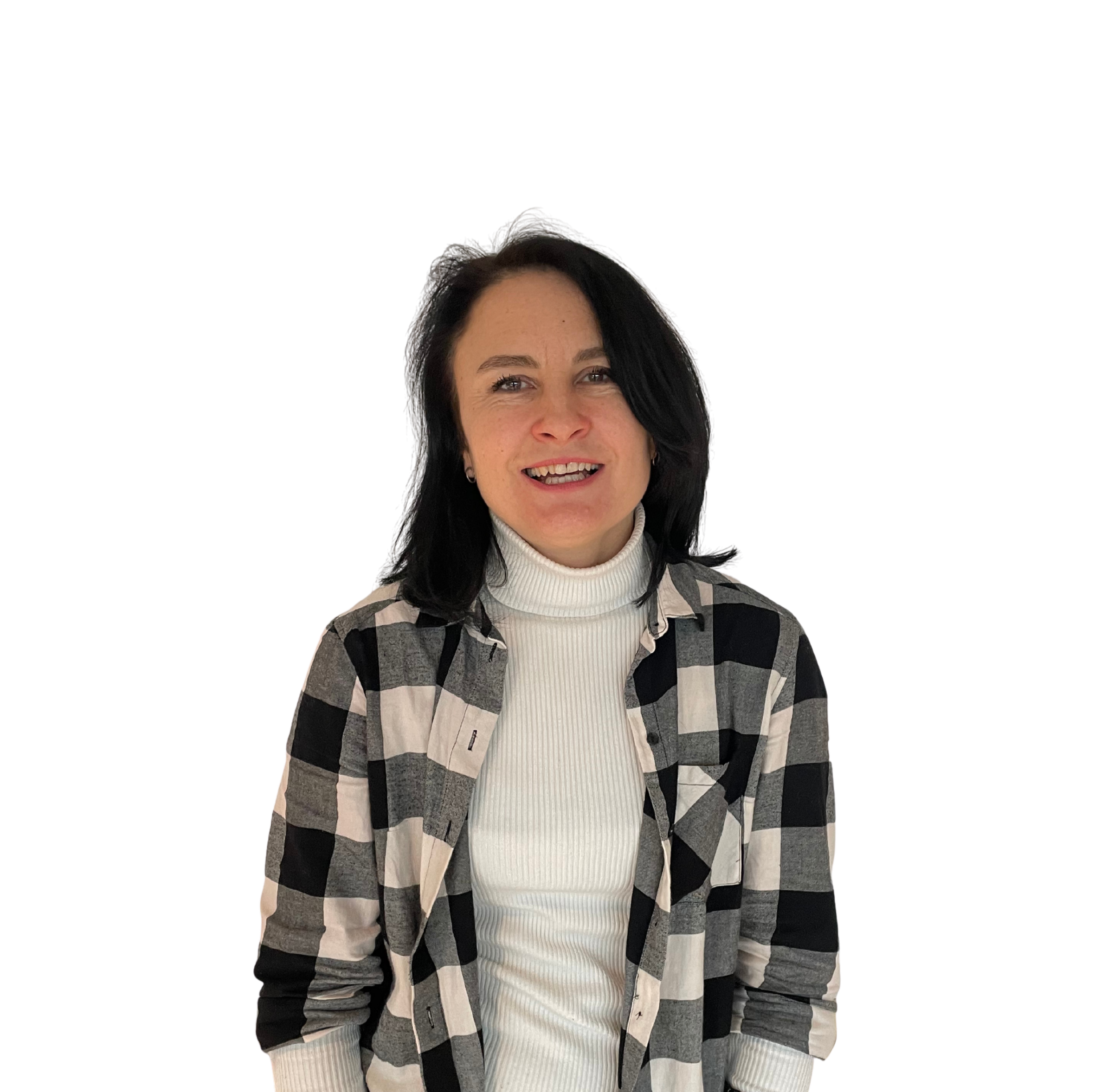 A woman with shoulder-length black hair smiling, wearing a white turtleneck and a black and white plaid shirt, standing against a black background.