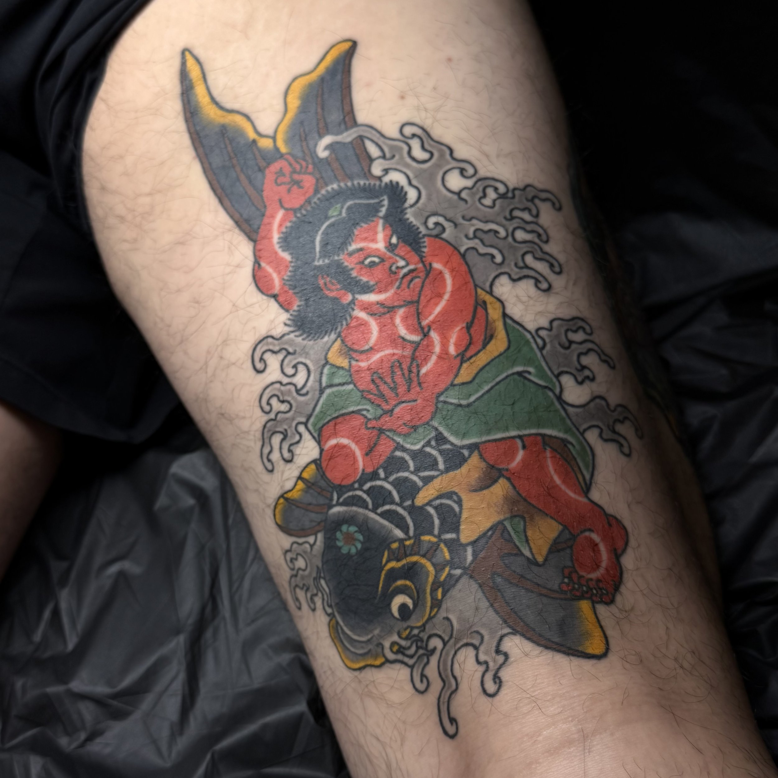 Traditional Japanese tattoo of Kintarō riding a black koi through waves, thigh piece