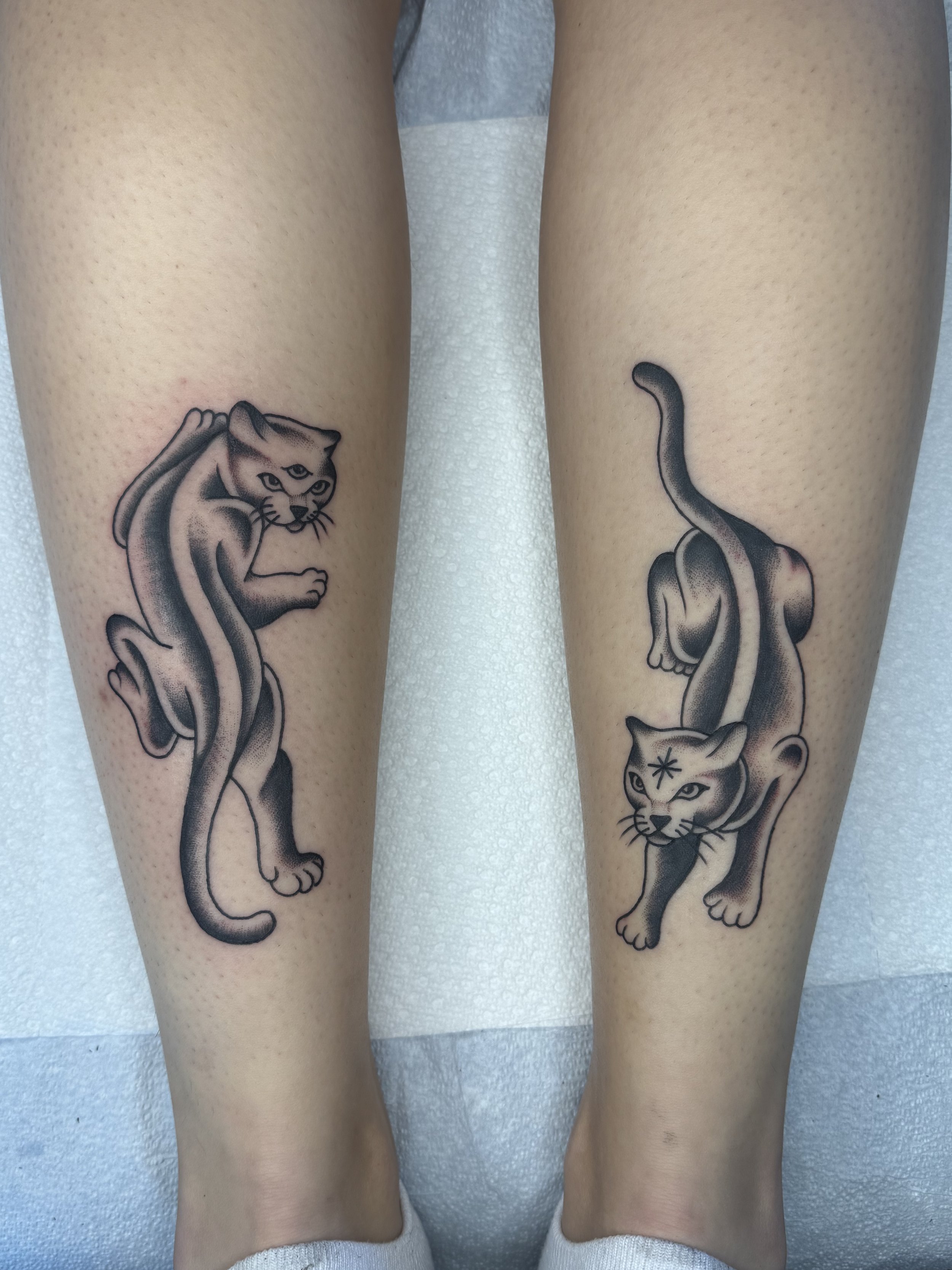 Tattoo artist Mel Gonzales, @theemelodic American Traditional black and gray matching panther tattoos on both legs at Dame of the West Tattoo in Scottsdale, Arizona.