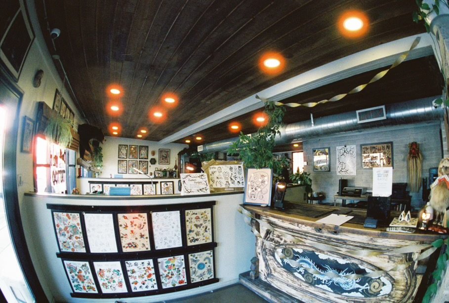 Dame of the West Tattoo shop interior showcasing framed tattoo flash designs on all of the walls, a decorated counter, green plants, and the occasional seasonal decorations.