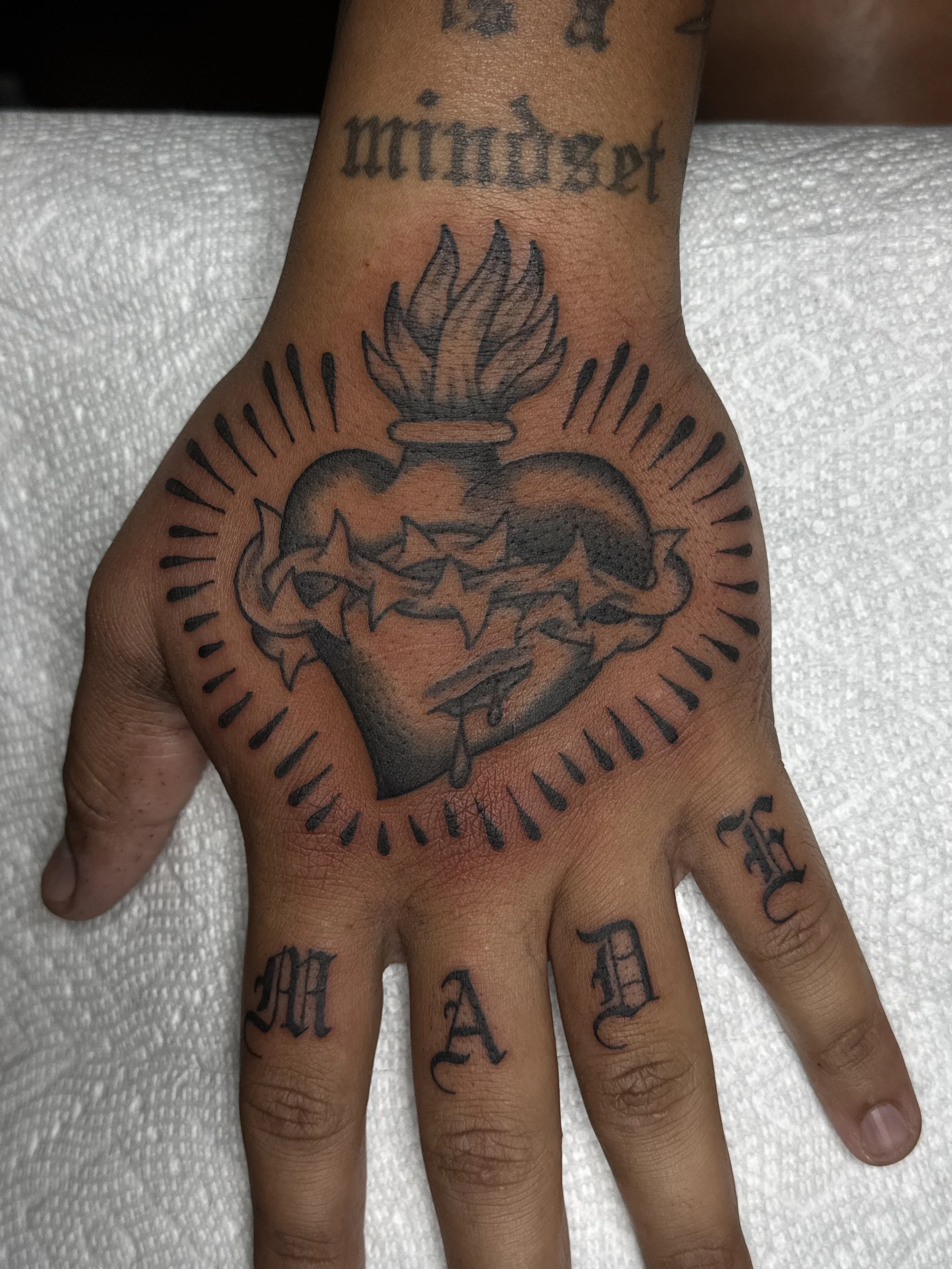 Tattoo artist Mel Gonzales, @theemelodic American Traditional black and gray sacred heart tattoo on the hand at Dame of the West Tattoo in Scottsdale, Arizona.
