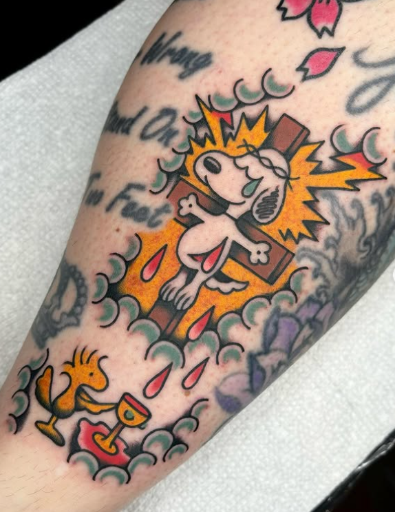 Chris Naderer American Traditional Full Color Crucified Snoopy tattoo on the leg tattooed at Dame of the West Tattoo in Scottsdale, Arizona