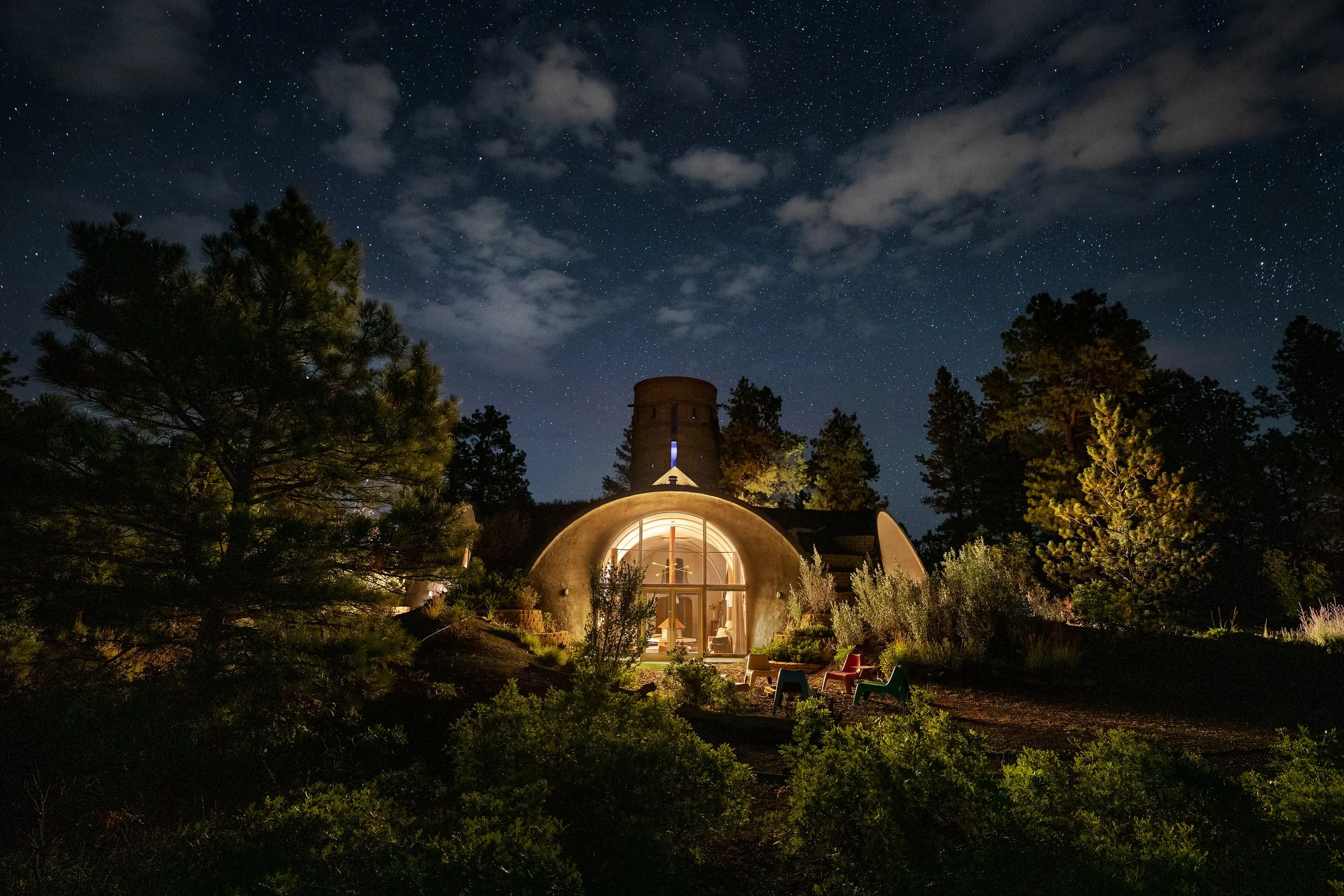 A cozy, lit dome-shaped house surrounded by trees under a starry night sky.