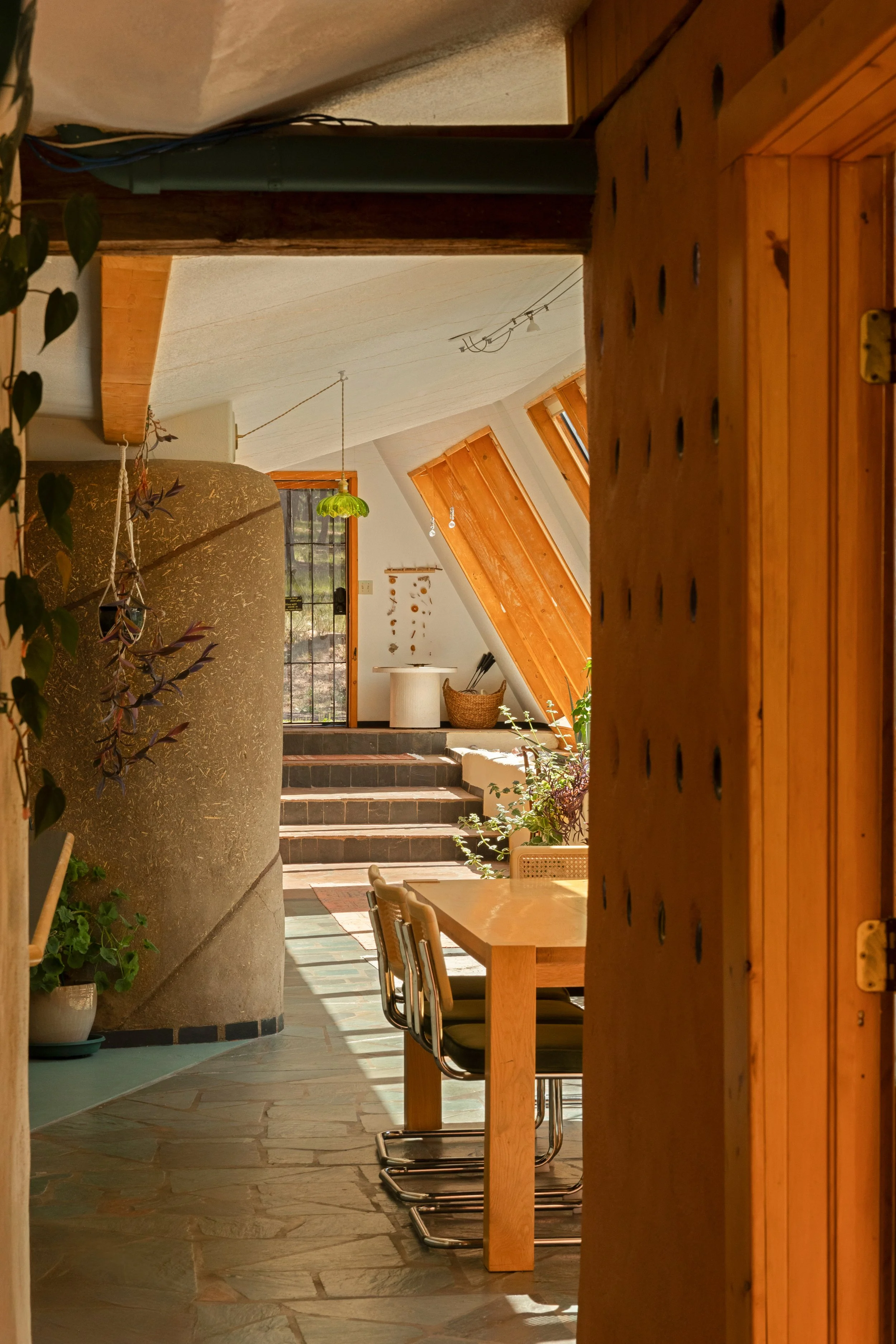 A cozy indoor space with wooden accents, a dining table with chairs, potted plants, and a staircase leading to an outdoor area.