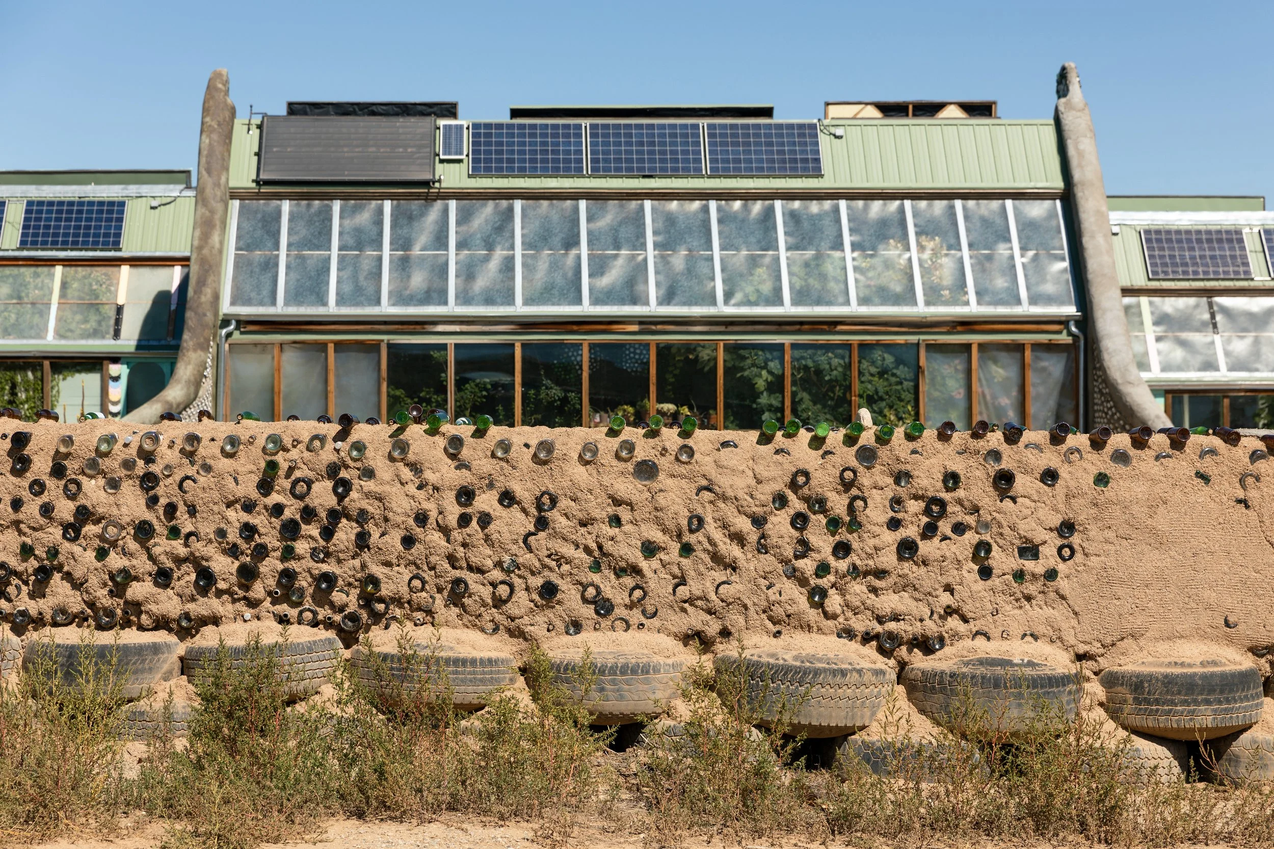 A building with solar panels on the roof and recycled bottles embedded in a dirt wall in front.