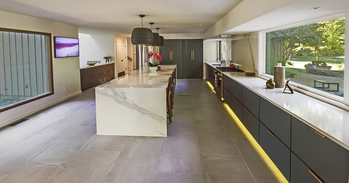 Modern East Memphis kitchen remodel featuring dark flat-panel cabinetry, waterfall island, large-format tile flooring, expansive windows and integrated under-cabinet lighting.