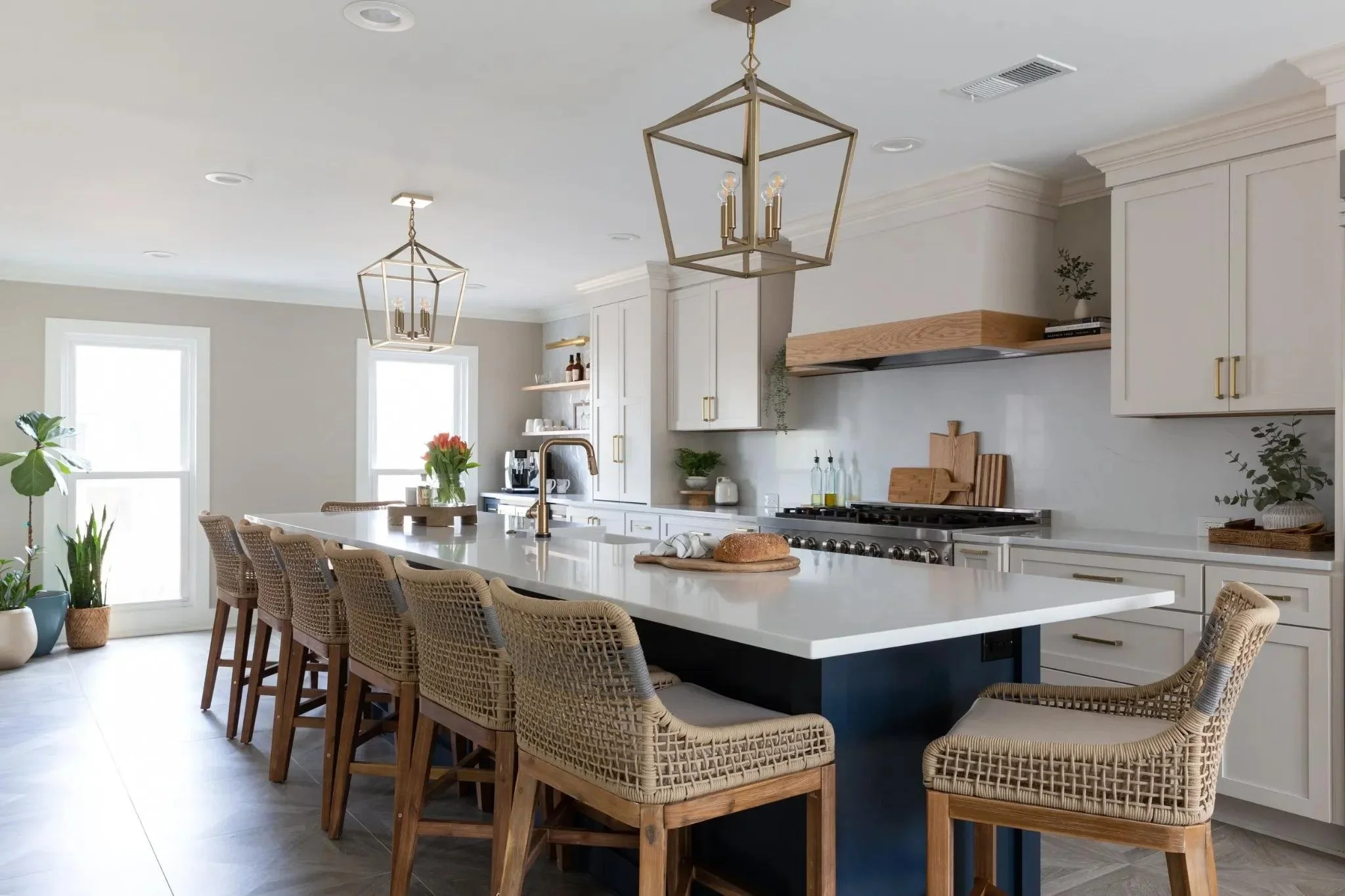 Luxury modern beige kitchen cabinetry with oversized navy kitchen island, woven bar stools, brass pendant lighting, and professional-grade appliances.