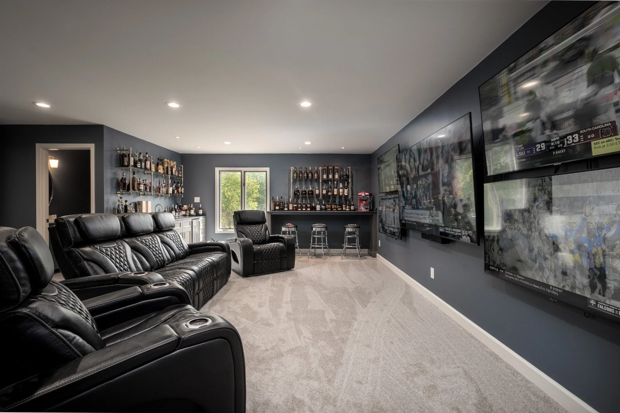 This custom mancave and media room remodel was designed for entertaining with oversized theater seating, multiple mounted televisions, moody blue walls, and a fully integrated custom bourbon bar.