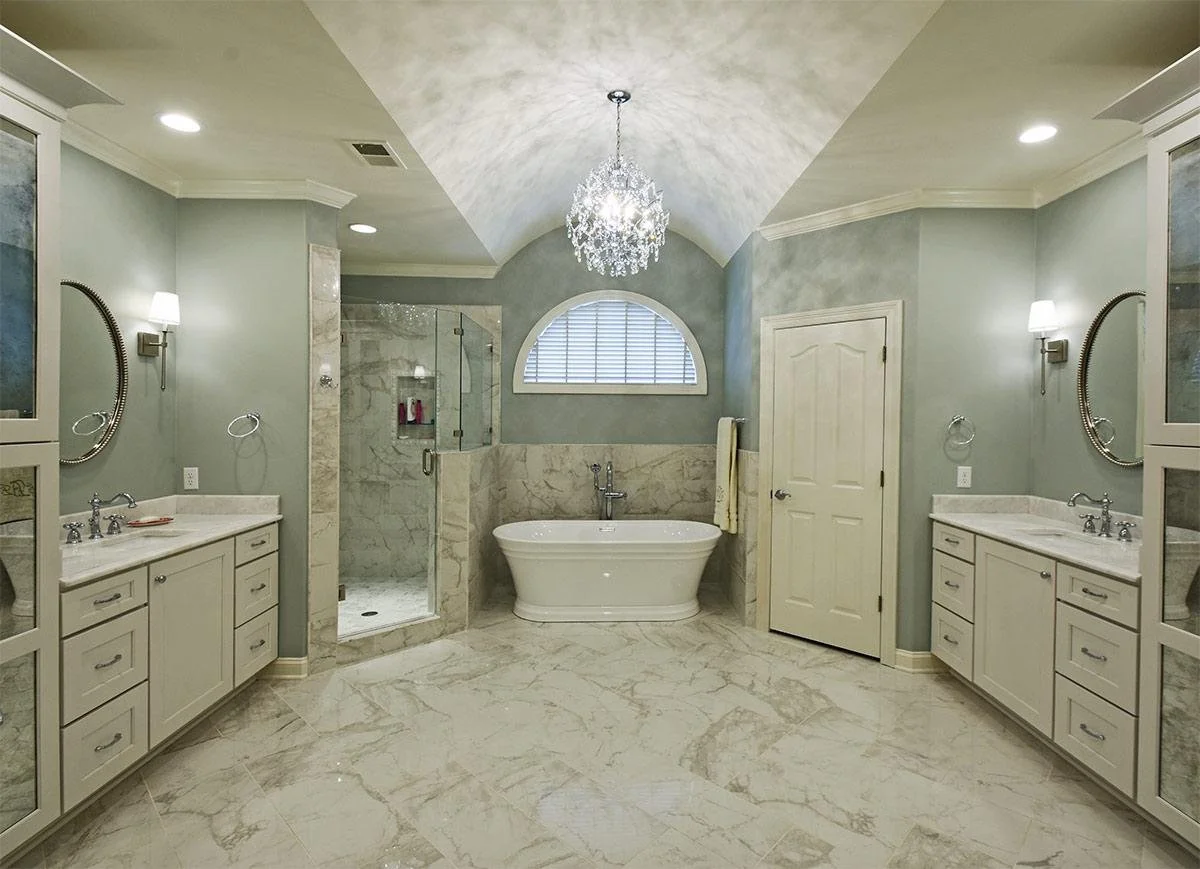 A freestanding soaking tub sits beneath an arched window, highlighted by a statement chandelier for a spa-like experience in this elegant primary bath.