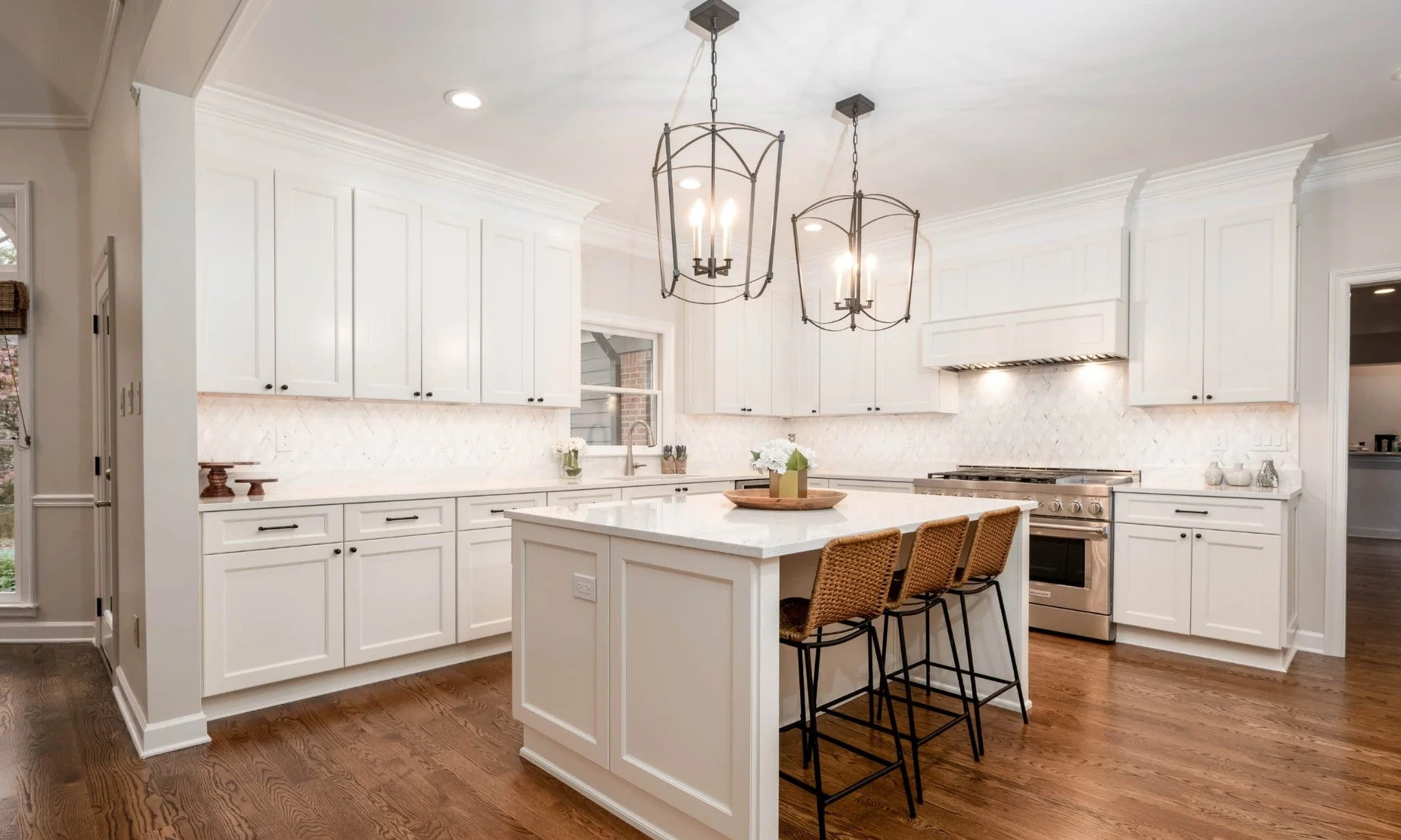 Bright white custom kitchen with marble backsplash, hardwood floors, custom cabinetry, and oversized island by Robbins Construction.