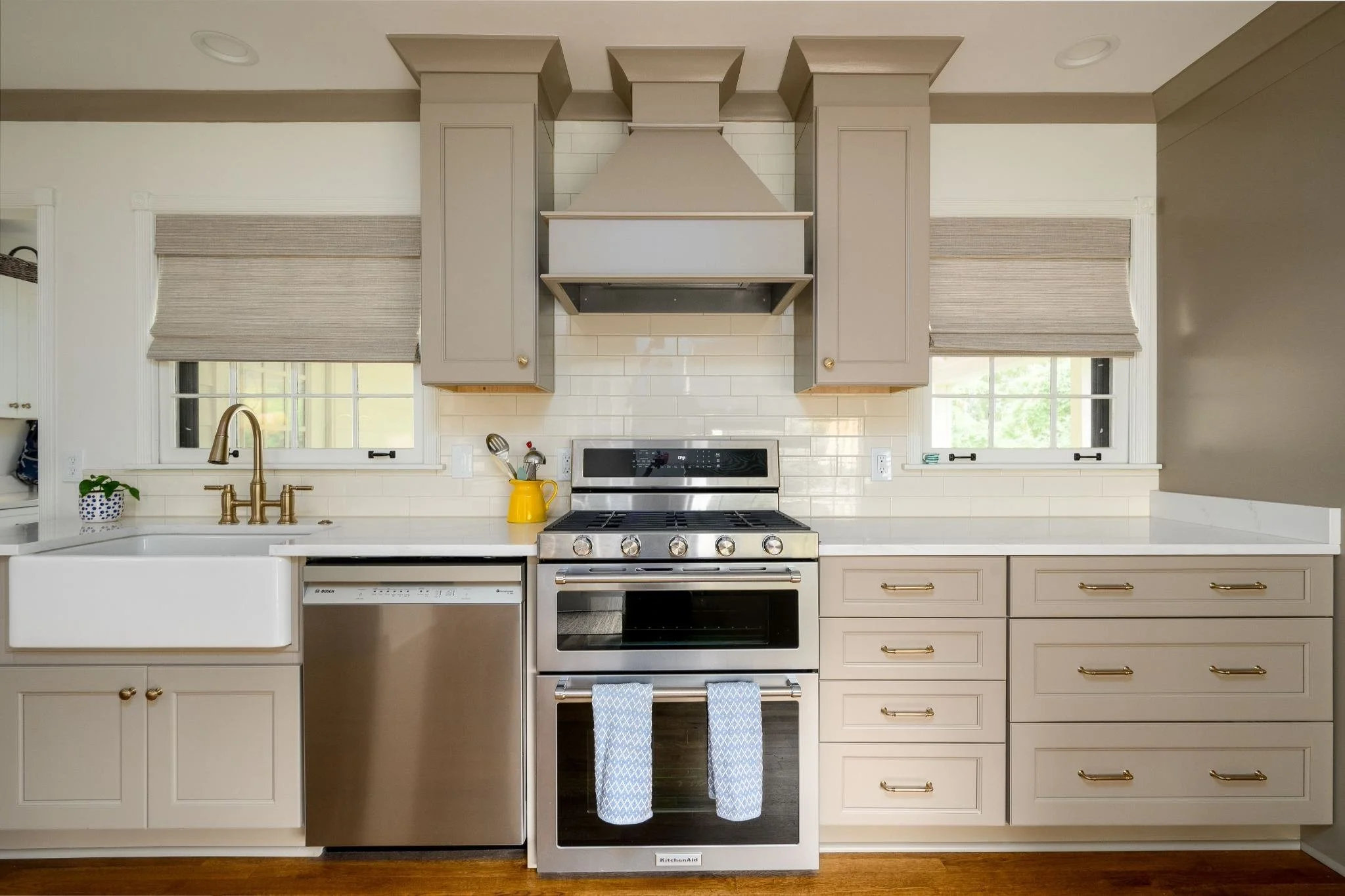 East Memphis kitchen remodel featuring taupe cabinets, a custom wood range hood, white subway tile backsplash and brass cabinet hardware.