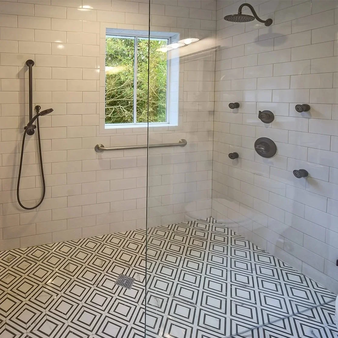 Aging-in-place bathroom with a spacious walk-in shower, built-in bench, handheld showerhead, grab bars, and slip-resistant patterned tile flooring.