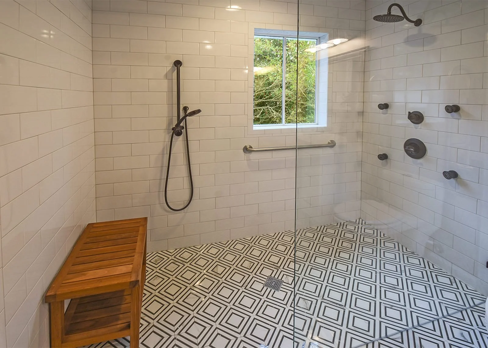 Modern accessible shower featuring white subway tile, multiple shower fixtures, grab bars, and barrier-free entry for aging-in-place living.