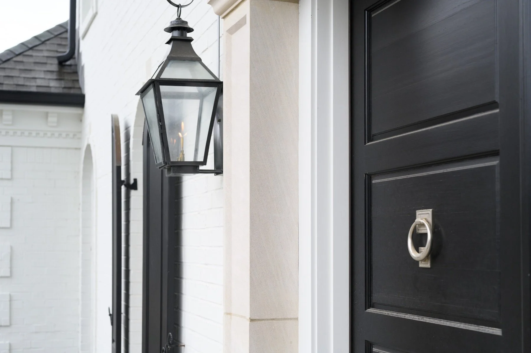 Elegant Germantown, TN home entrance featuring a black front door with decorative metal knocker, white brick exterior, and traditional black lantern lighting.