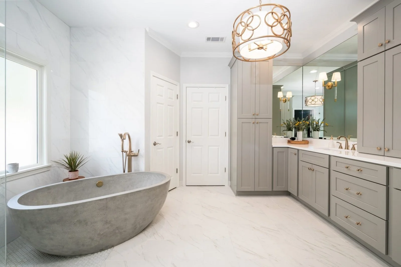 Germantown primary bathroom with a freestanding concrete soaking tub, custom gray cabinetry and coordinated brass fixtures.