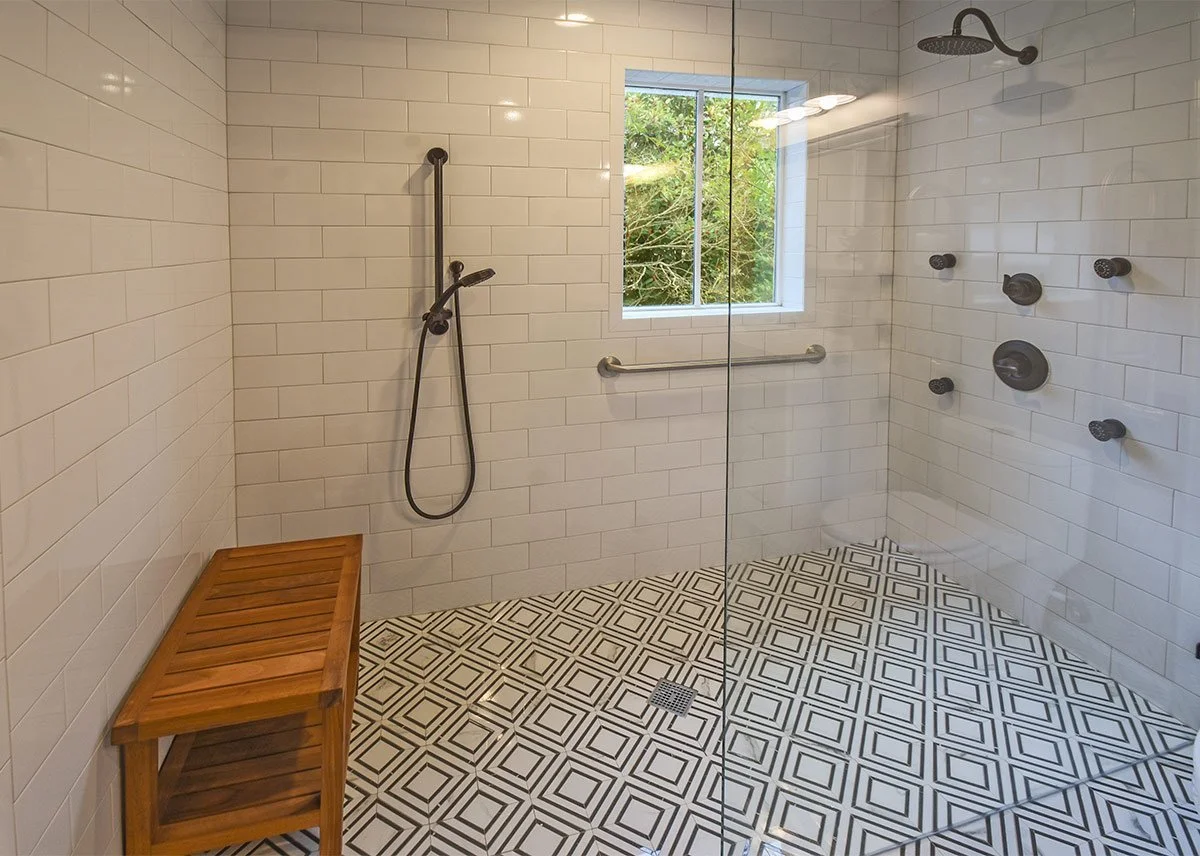 Accessible bathroom renovation with a curbless walk-in shower, built-in bench, grab bars, handheld showerhead, and patterned tile floor.