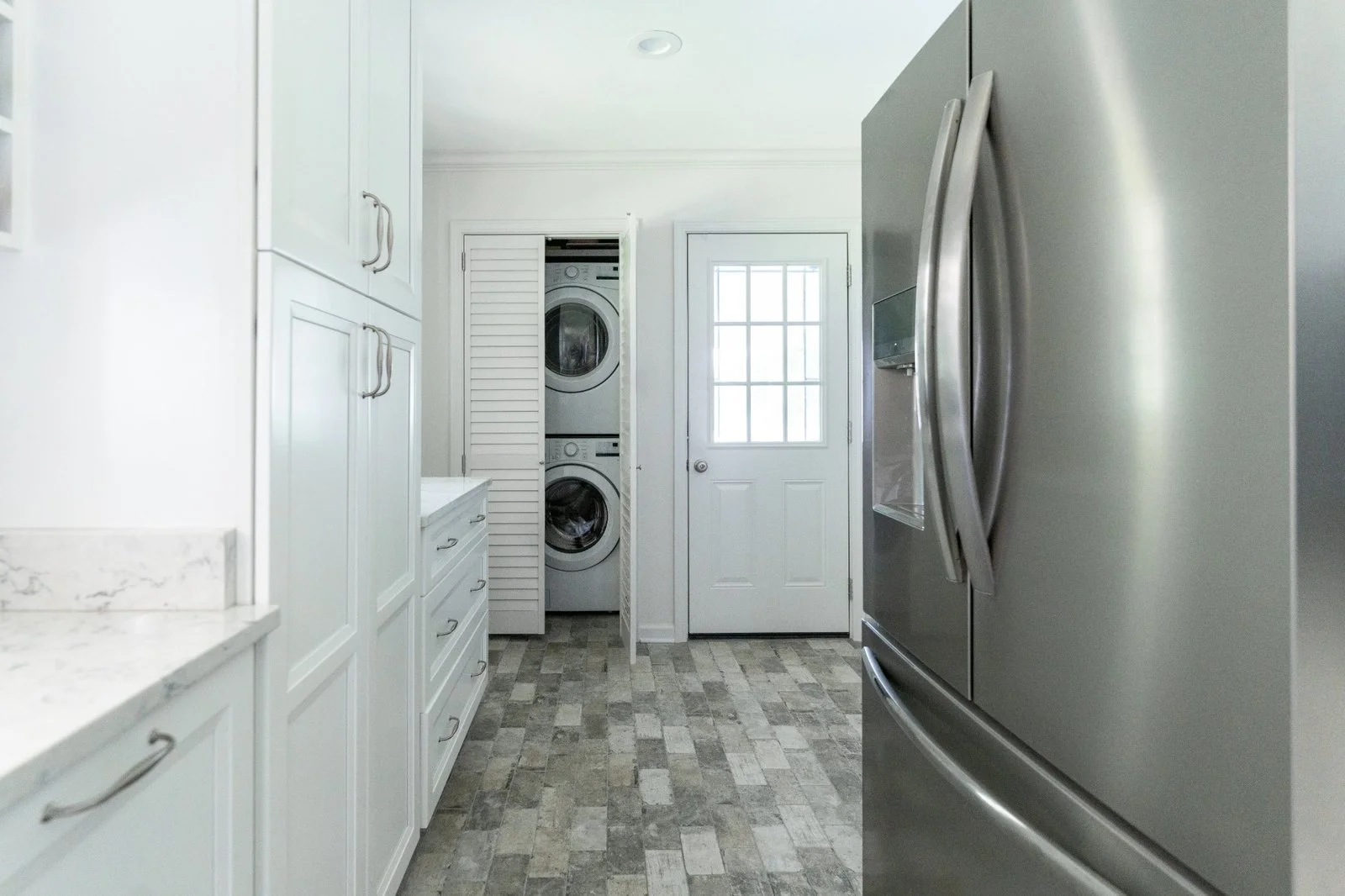 Clean laundry room with white cabinets, stacked washer and dryer, and stainless steel refrigerator.