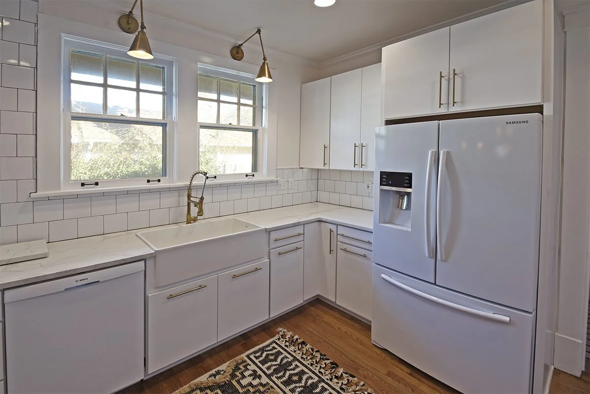Kitchen with white cabinets, white subway tile backsplash, white countertops, a white farmhouse sink, a Samsung refrigerator with water and ice dispenser, a window above the sink, and hardwood flooring, with a patterned rug on the floor.