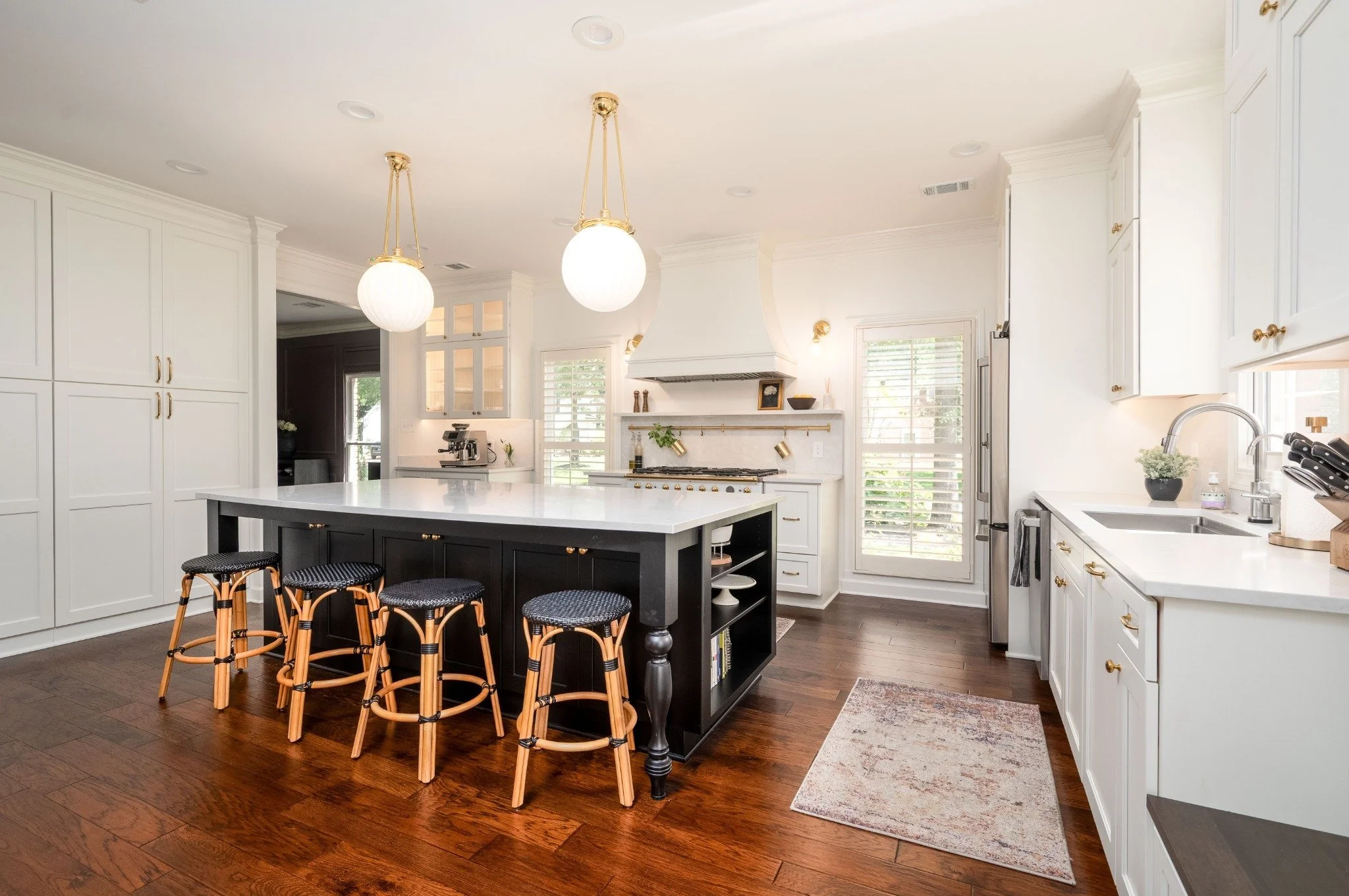 Bright, modern kitchen with white cabinets, a large black island with seating, hardwood floors, and pendant lighting.