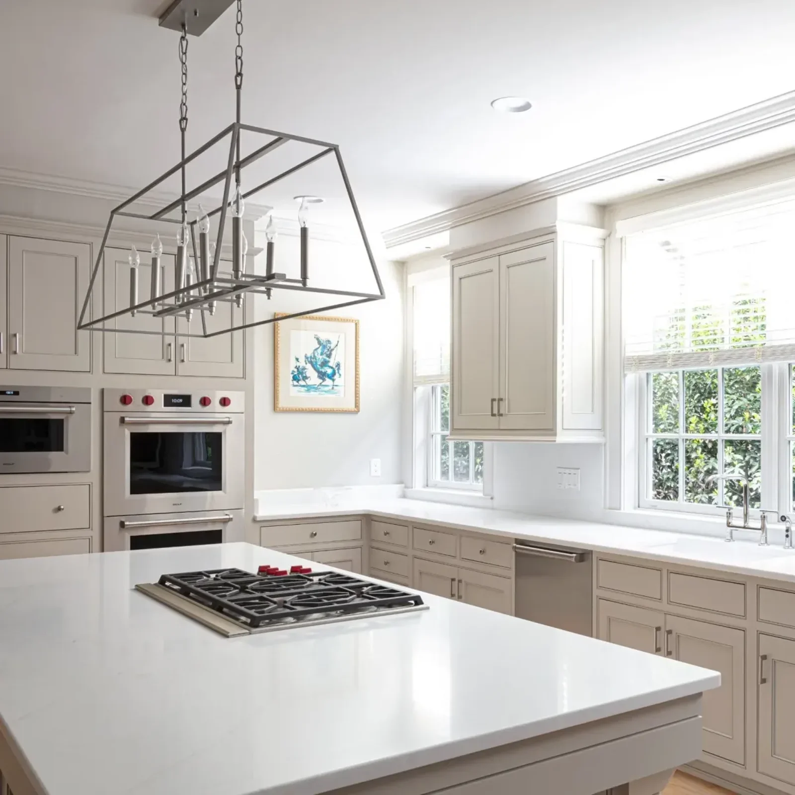 Modern white kitchen with large island, built-in oven, gas cooktop, pendant light fixture, and large windows with blinds.