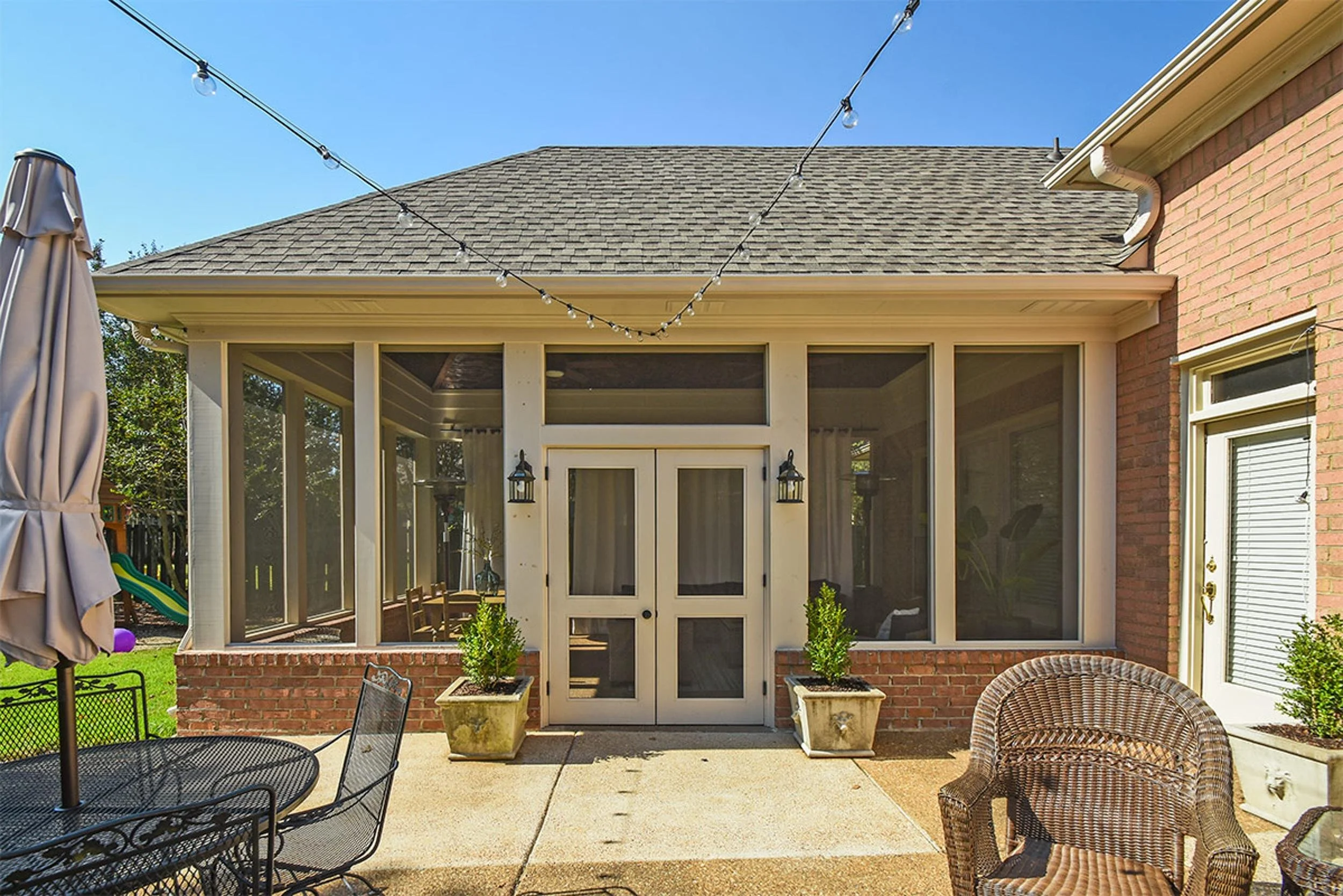 Backyard patio area with outdoor furniture, string lights, and a screened-in porch with glass doors.