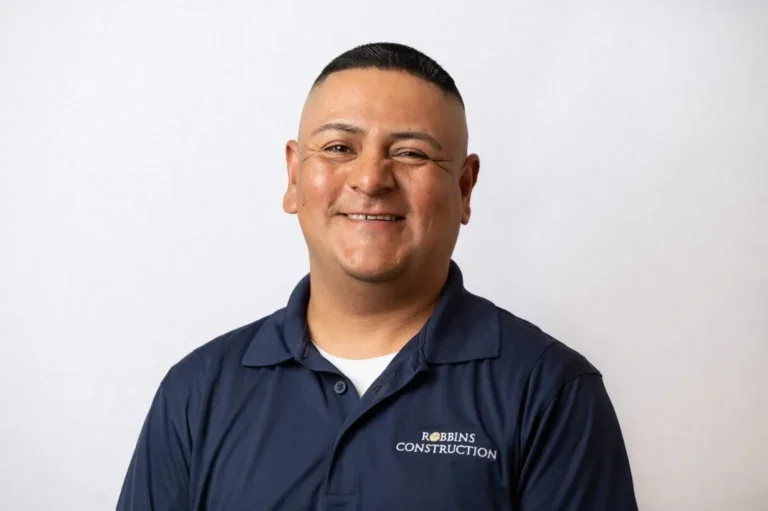 A man in a navy blue polo shirt with Robinsons Construction logo, smiling and standing against a light background.