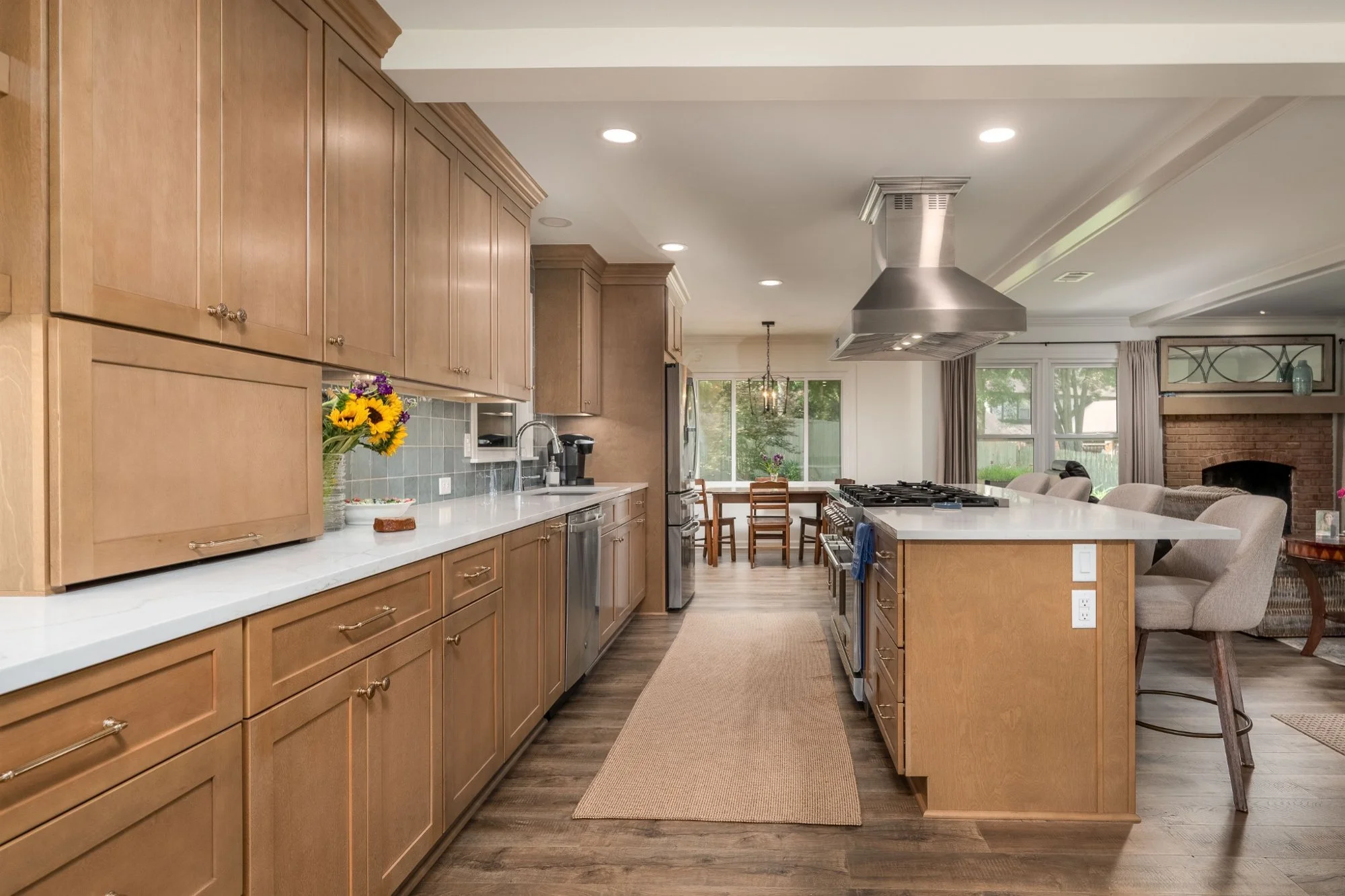 Open-concept kitchen remodel with natural wood cabinetry, white countertops, a large cooking island, and adjoining living and dining spaces.