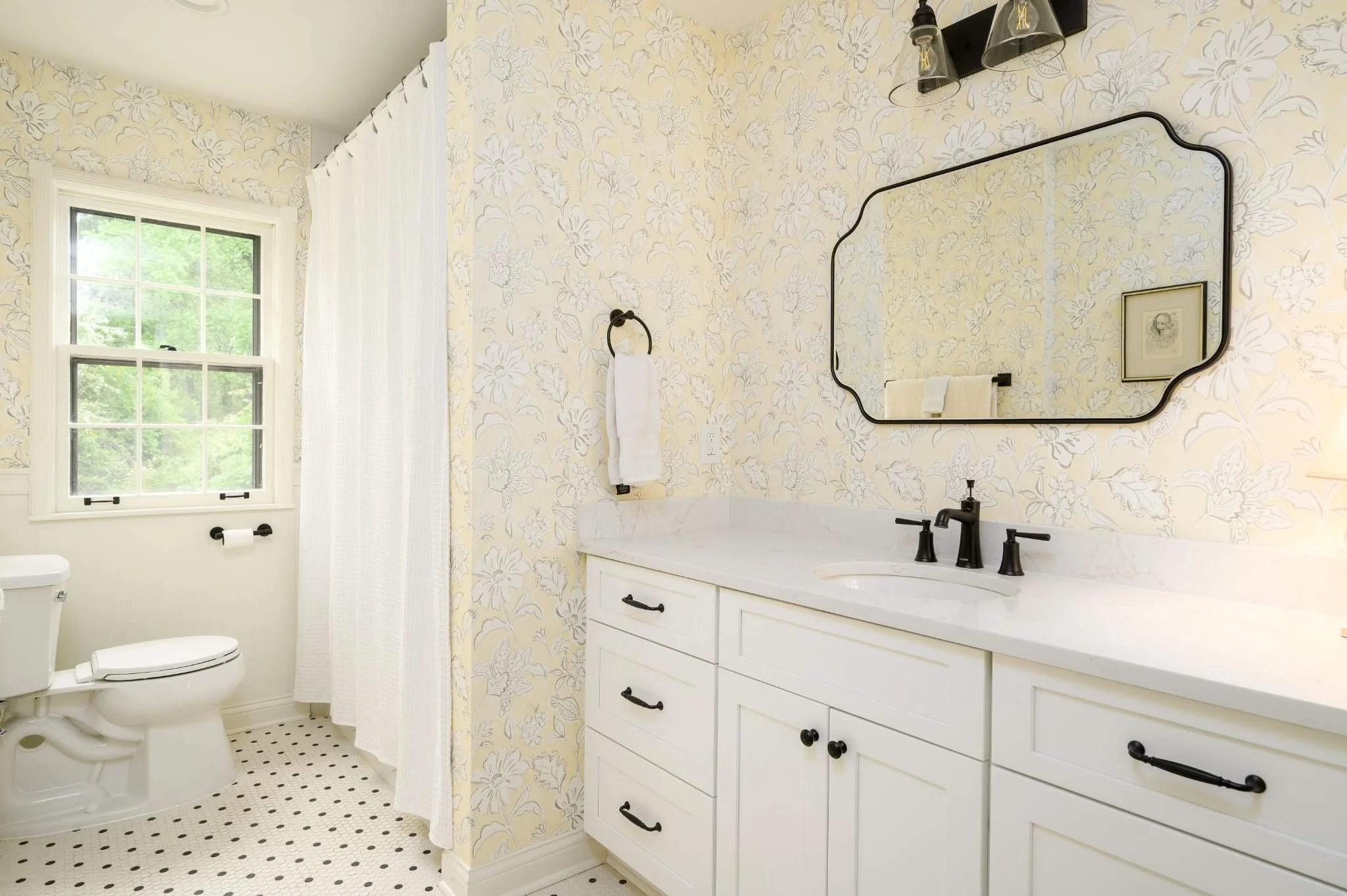 Hall bathroom remodel in East Memphis featuring soft floral wallpaper, a white vanity, black fixtures, mosaic tile flooring and a bright window.