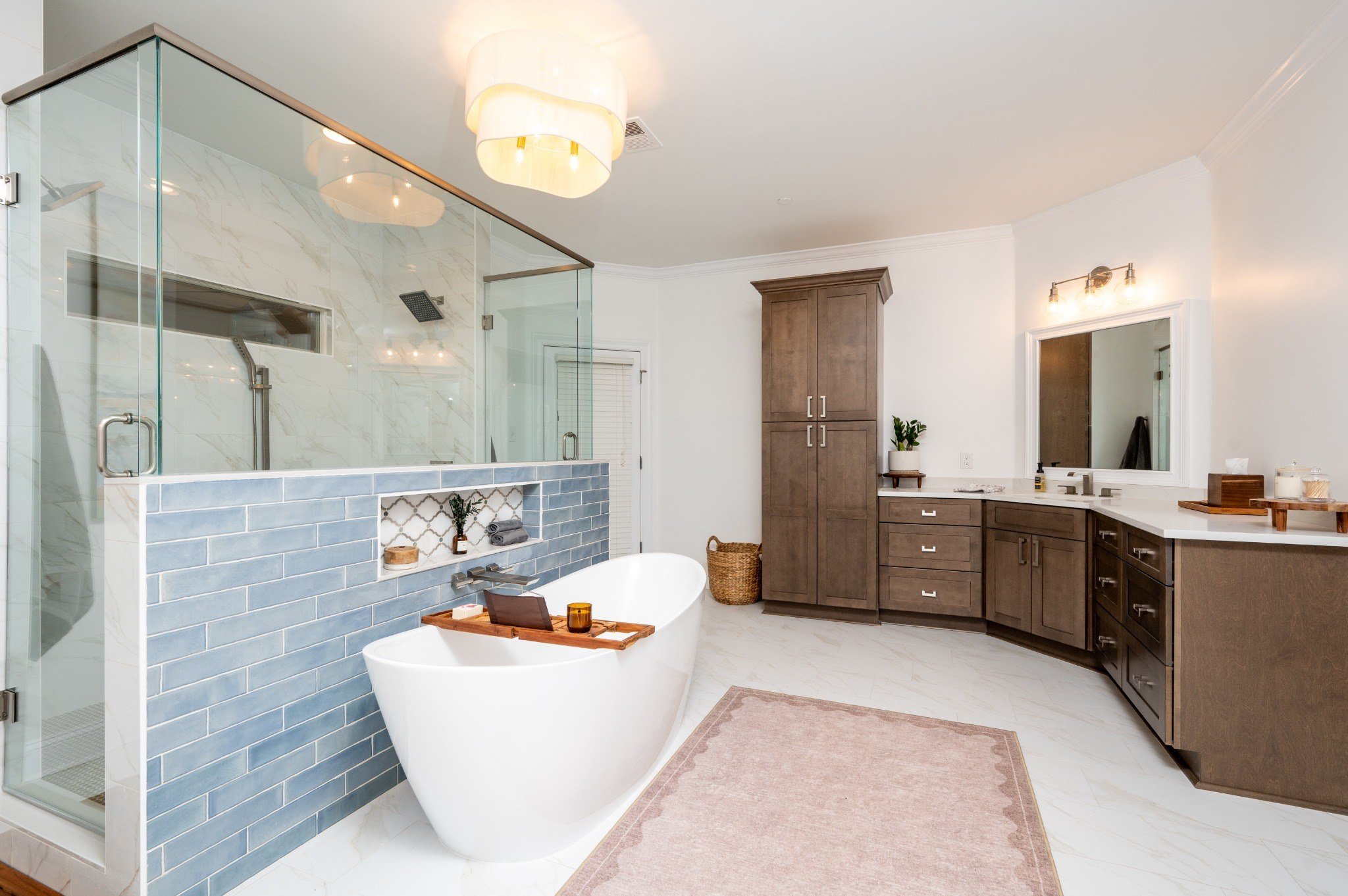 Modern bathroom with a white freestanding bathtub, glass-enclosed shower with marble walls, wooden cabinetry, and a large mirror above the vanity.