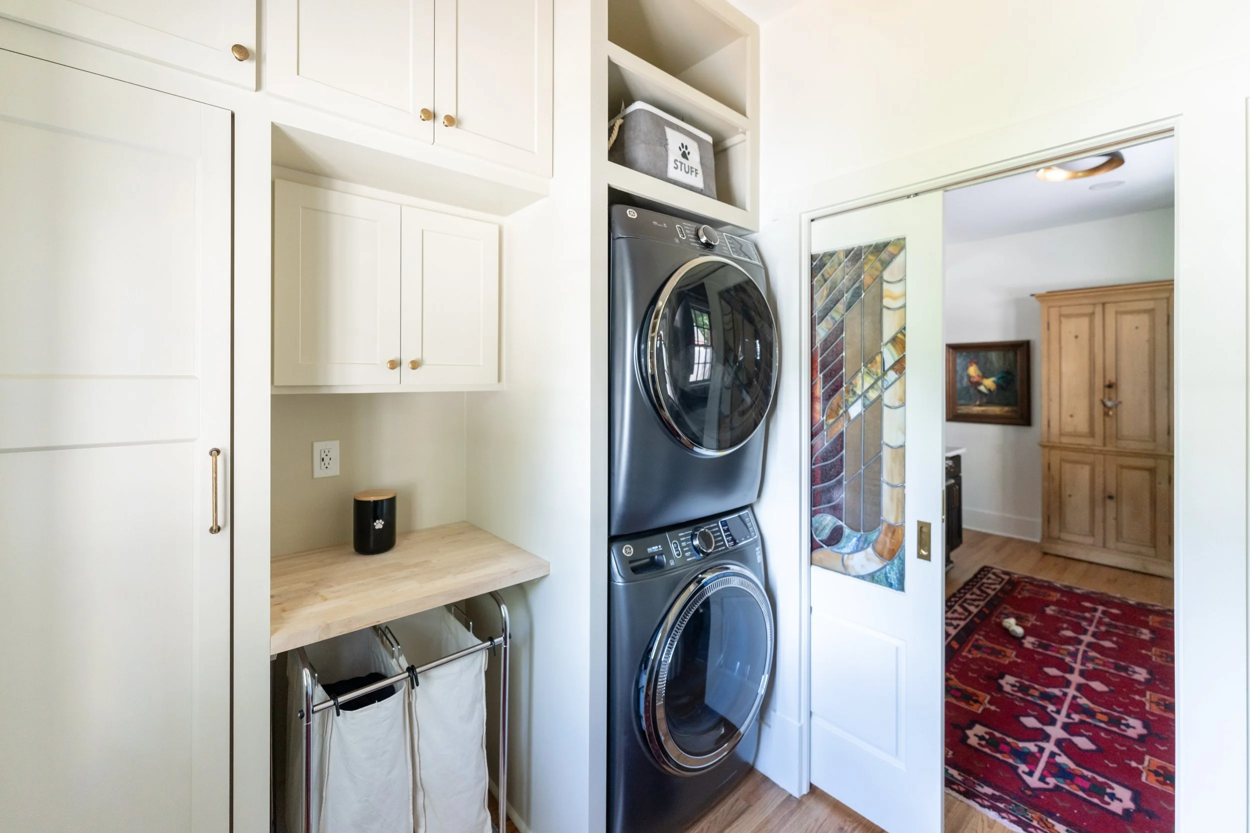 Custom laundry room with stacked washer and dryer, white cabinetry, folding counter, built-in hampers, and a decorative sliding door.