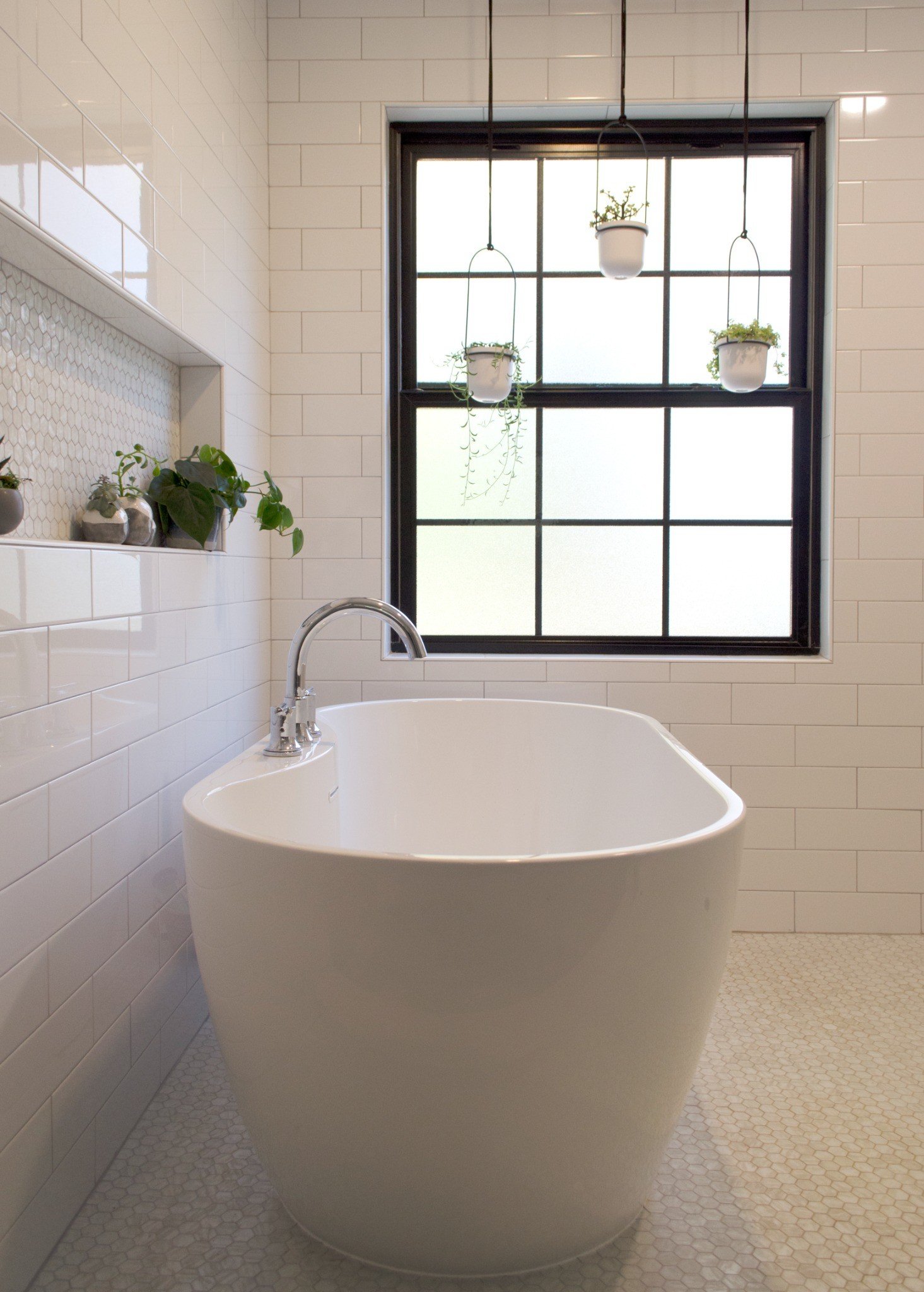 The freestanding soaking tub is paired with a recessed tile niche featuring textured hexagon tile accents and decorative greenery.