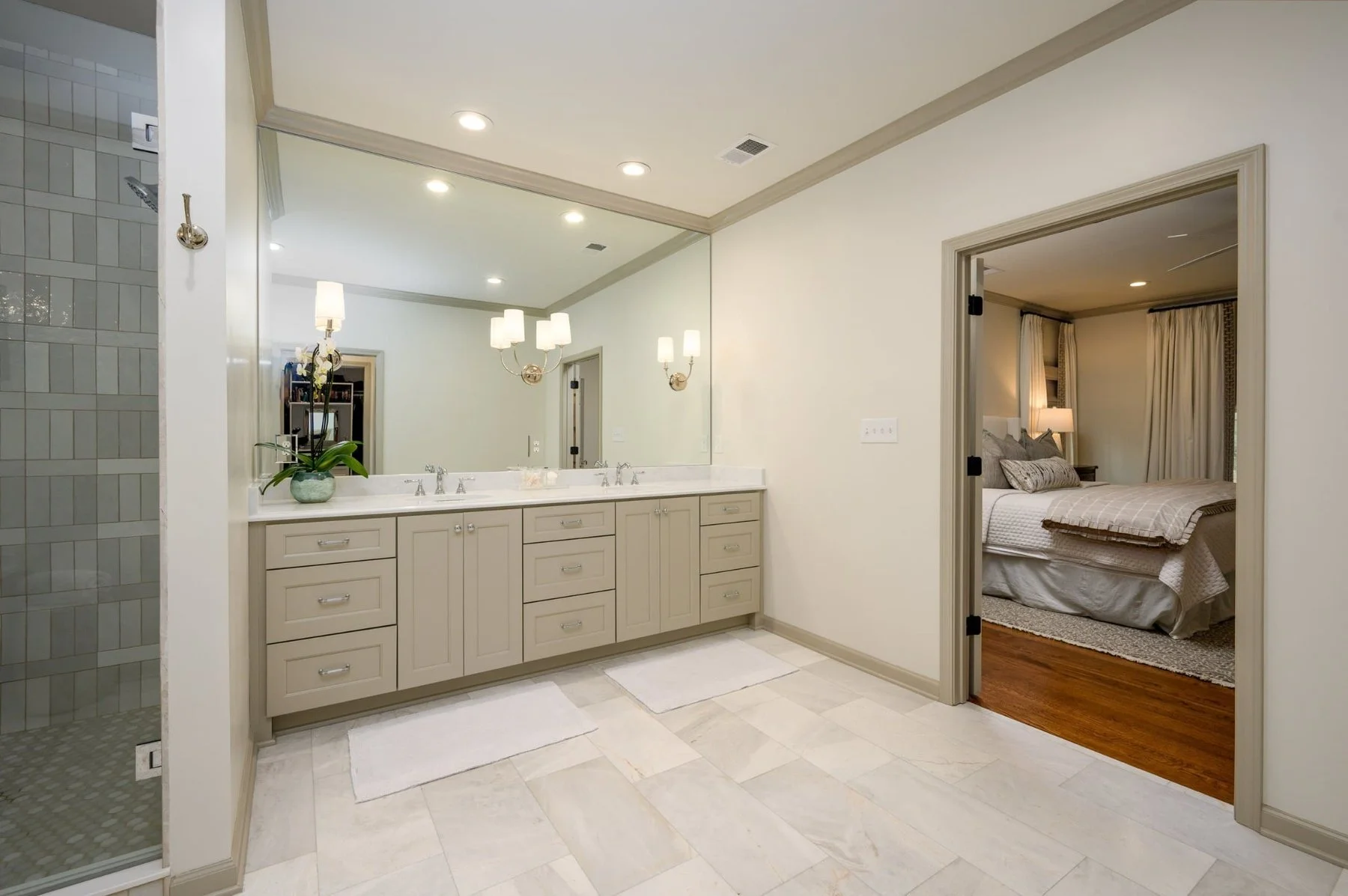 Remodeled primary bathroom in East Memphis featuring a custom double vanity, wall-to-wall mirror, walk-in tile shower and an open connection to the primary bedroom.